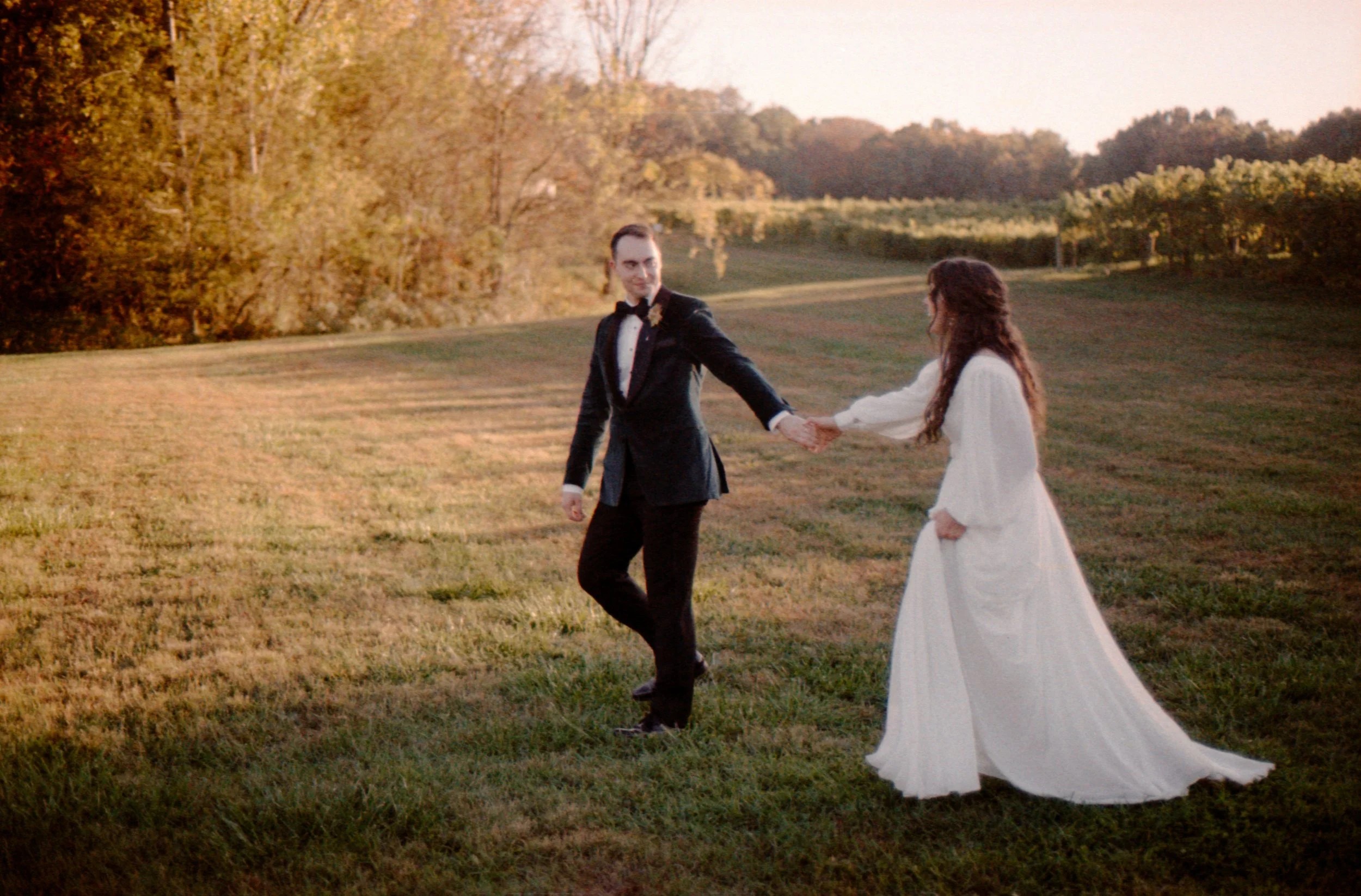 LBW95-groom-leading-bride-on-grass-sunset.jpg