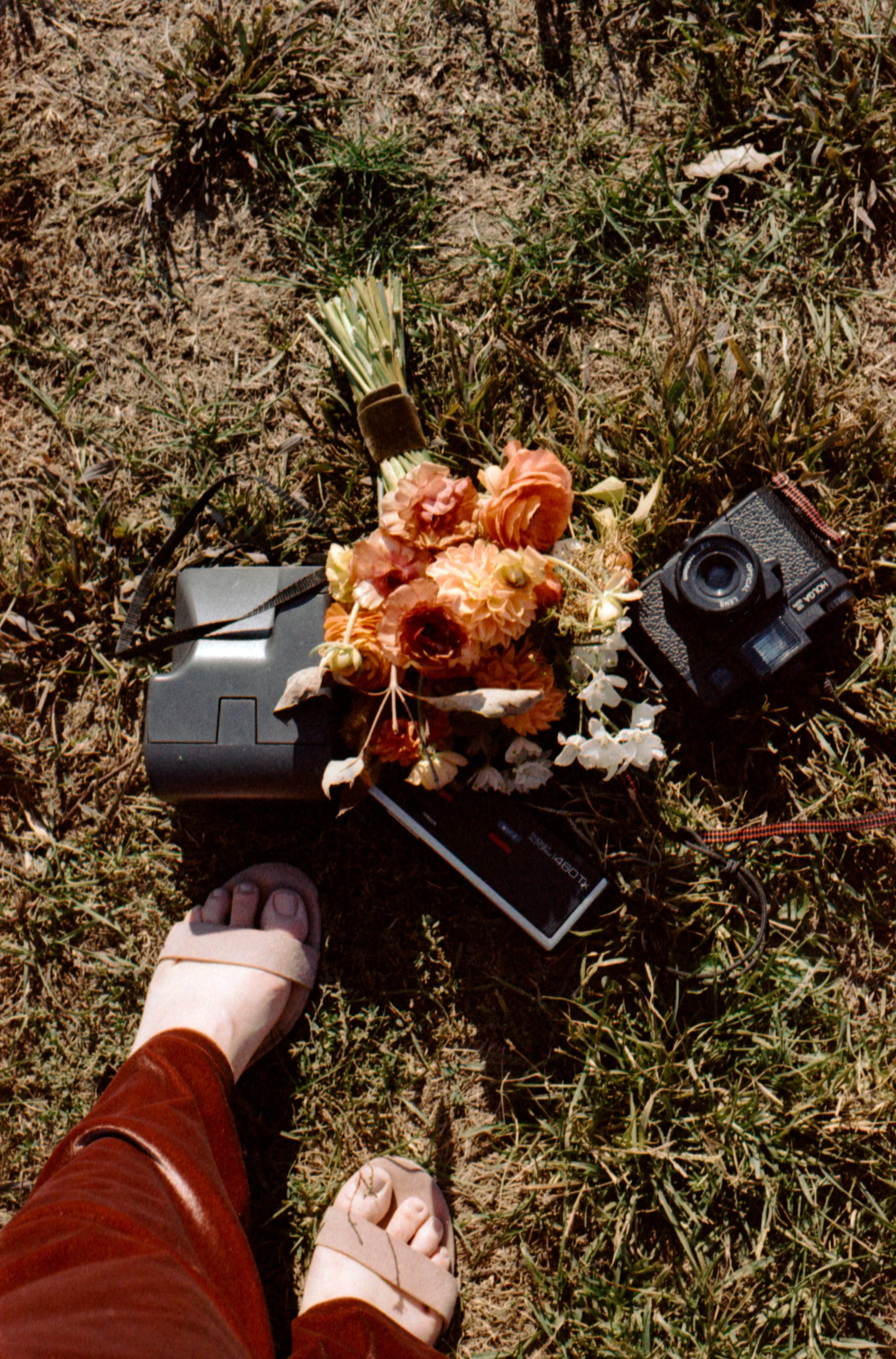 LBW86-woman-standing-by-cameras-on-grass-with-flower-bouquet.jpg