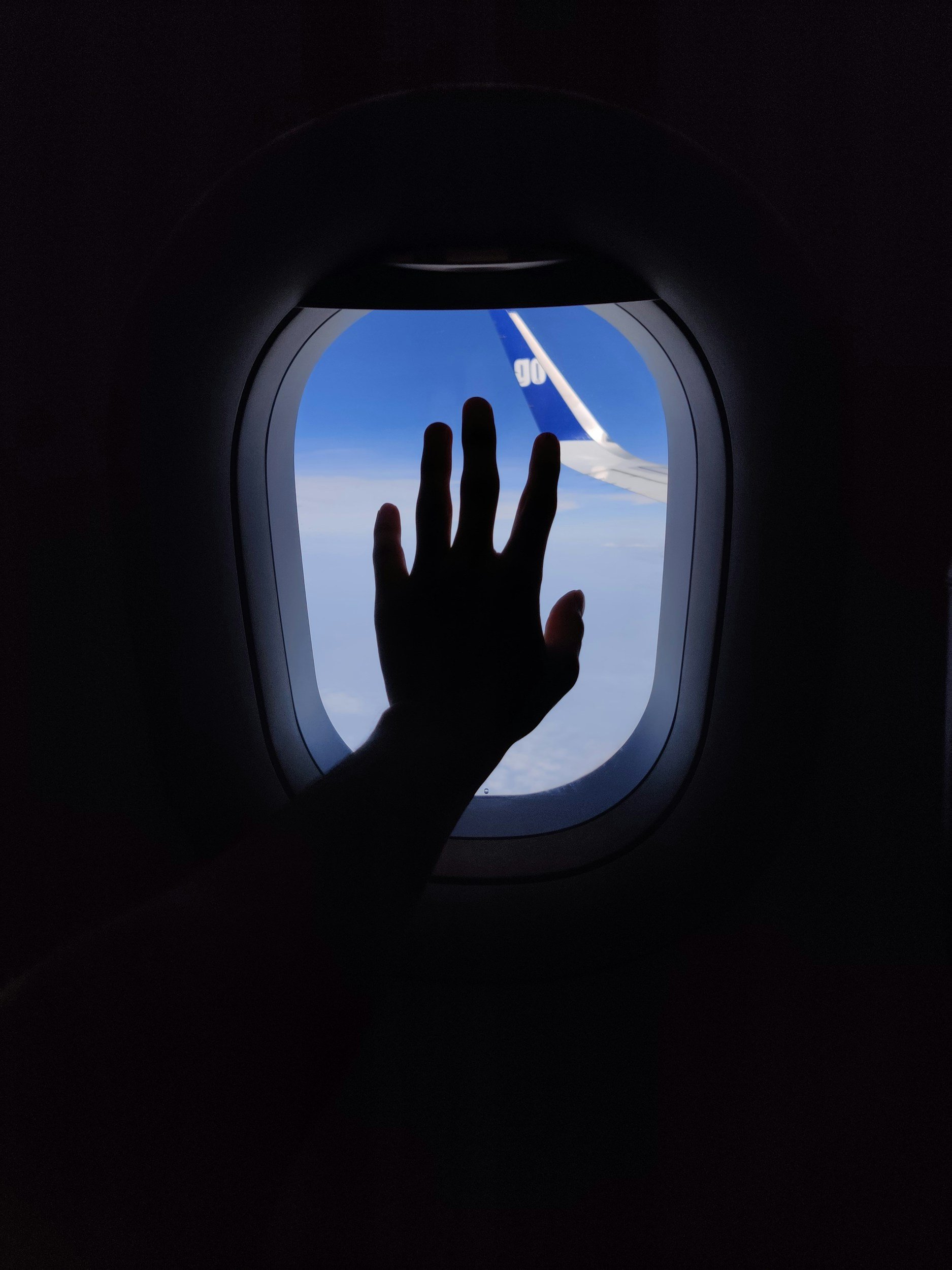 Person reaching out to touch the window of an airplane with a view of the sky and the tail of another airplane outside.