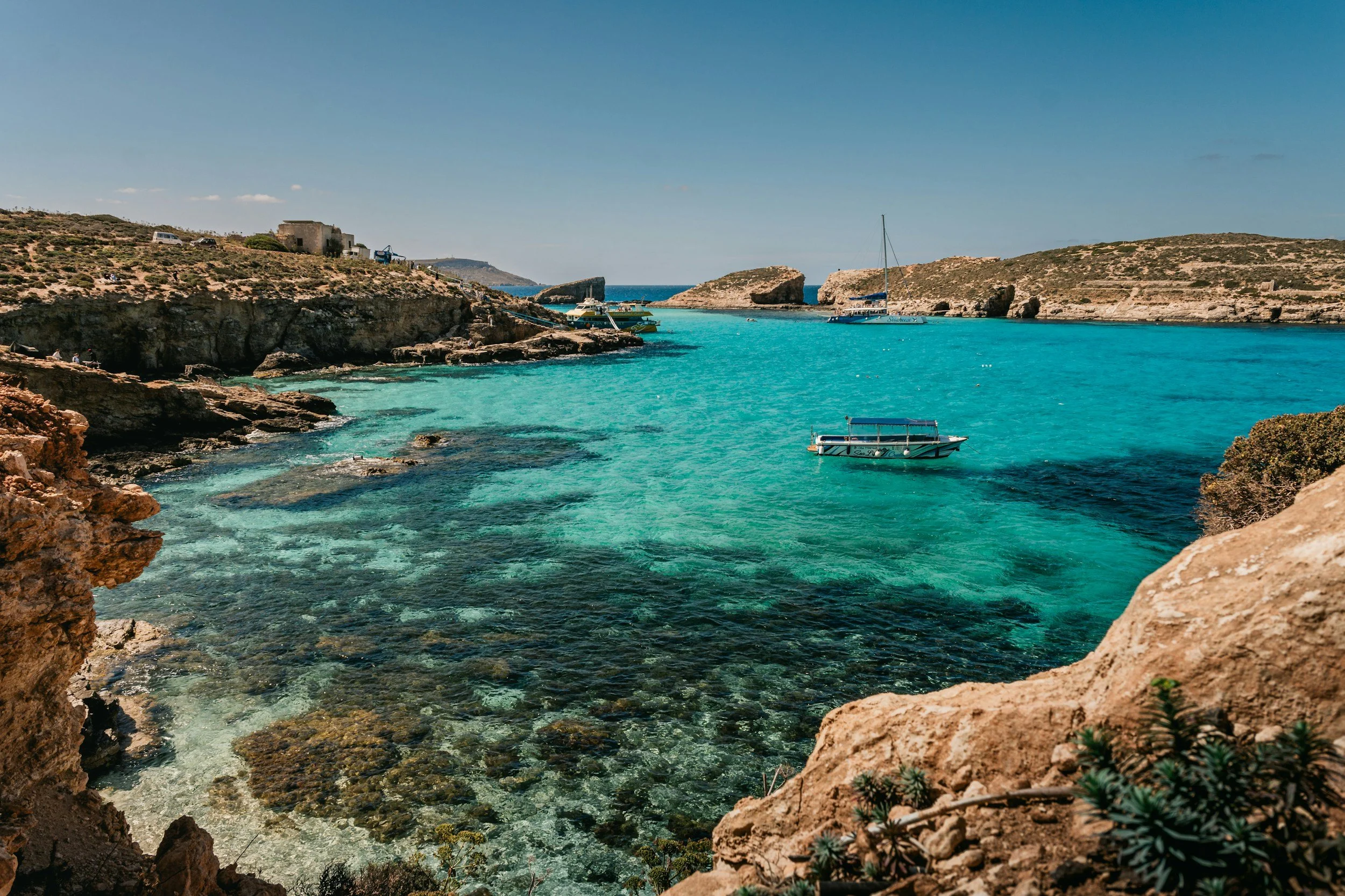 Turquoise water in a cove with boats, rugged cliffs, and clear skies.
