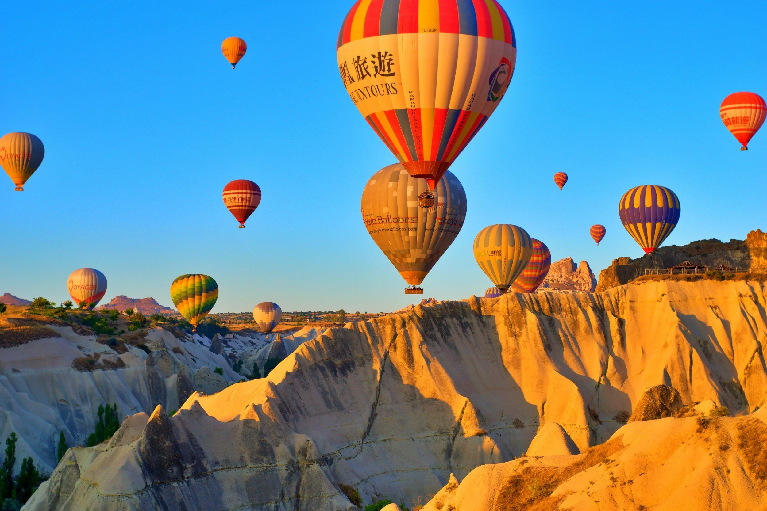 Hot air balloons floating over a rocky, mountainous landscape at sunrise or sunset.