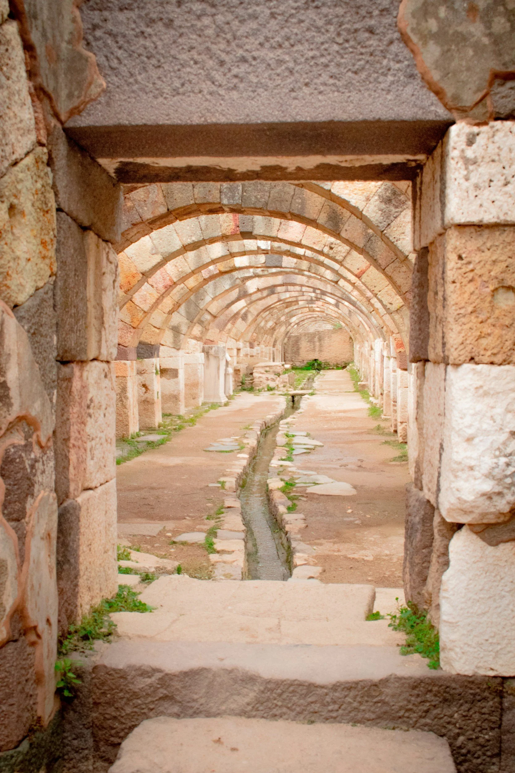 Ancient stone ruins with a series of arches and a small water channel running through the middle, seen through a stone doorway.