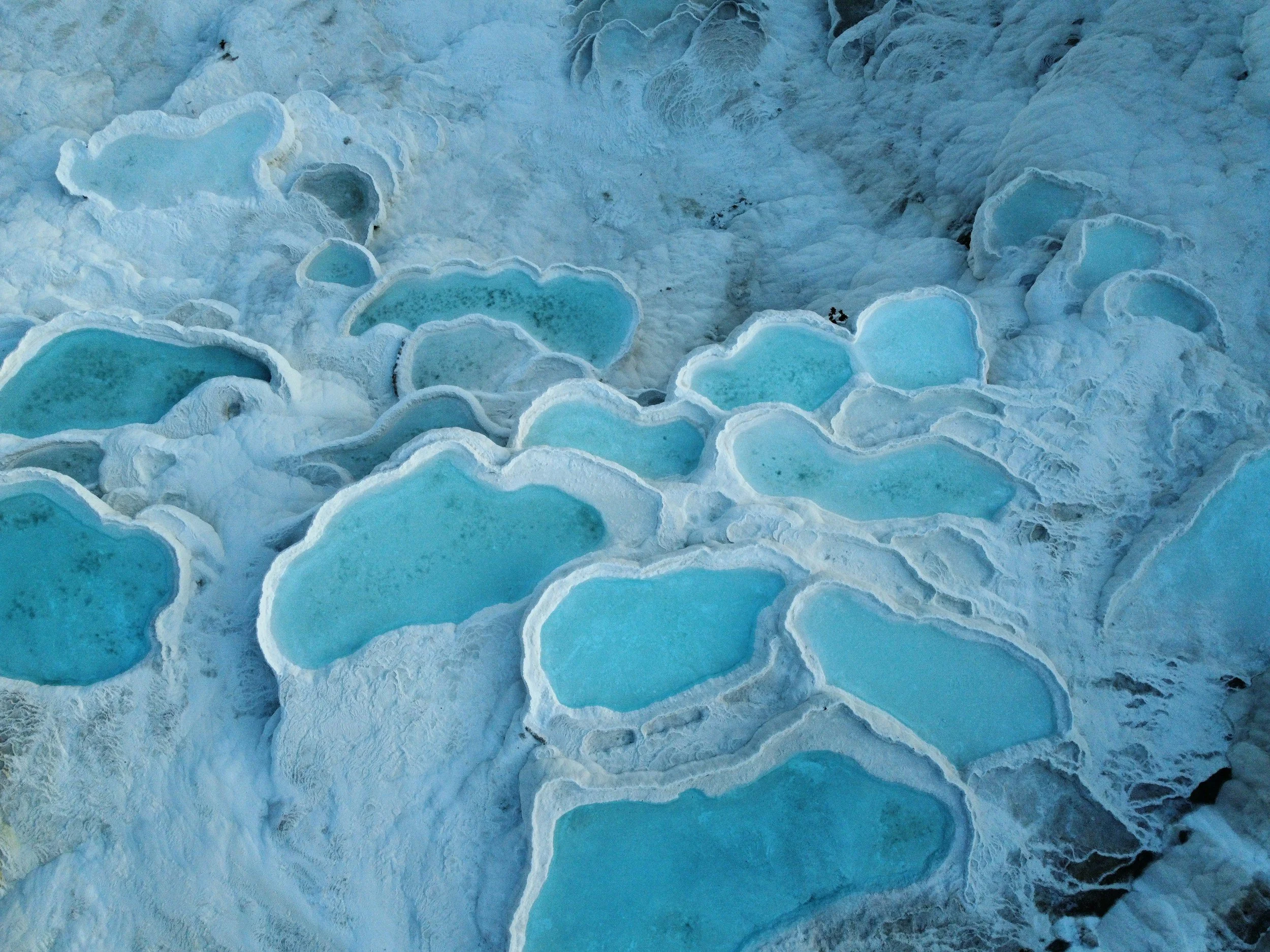 Aerial view of blue ice pools and formations in a snowy landscape.