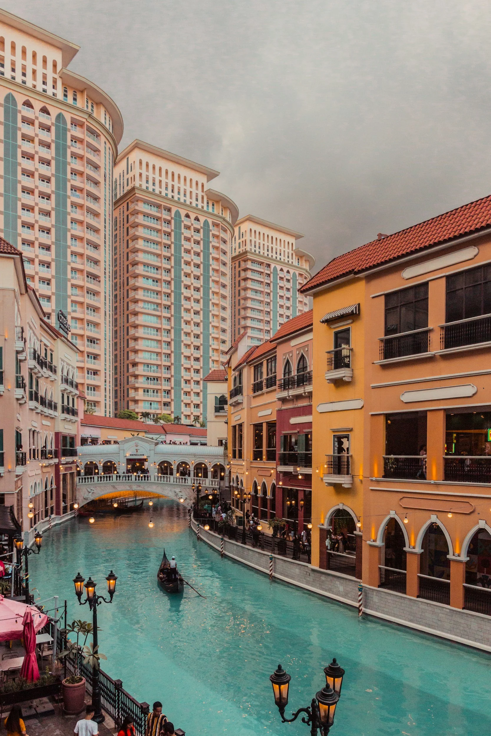 Colorful European-style buildings lining a canal with a gondola and bridge, under a cloudy sky.
