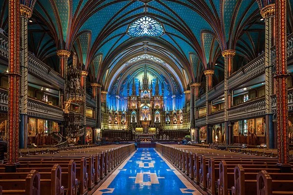 Interior of a grand, ornate church with high vaulted ceilings, elaborate decorations, and pews on both sides of a central aisle.