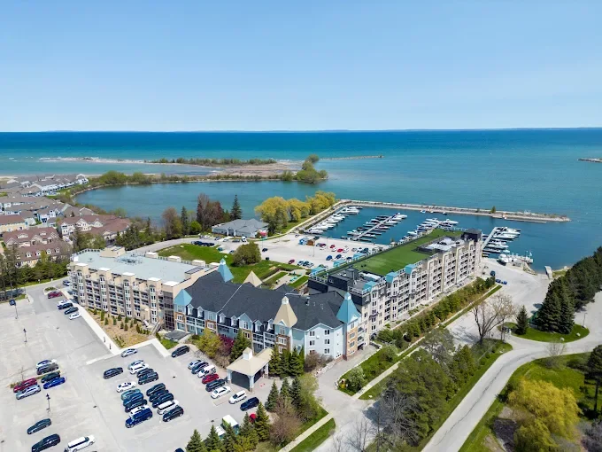 Aerial view of a waterfront apartment complex with parking lots, a marina with boats, and a large body of water in the background.