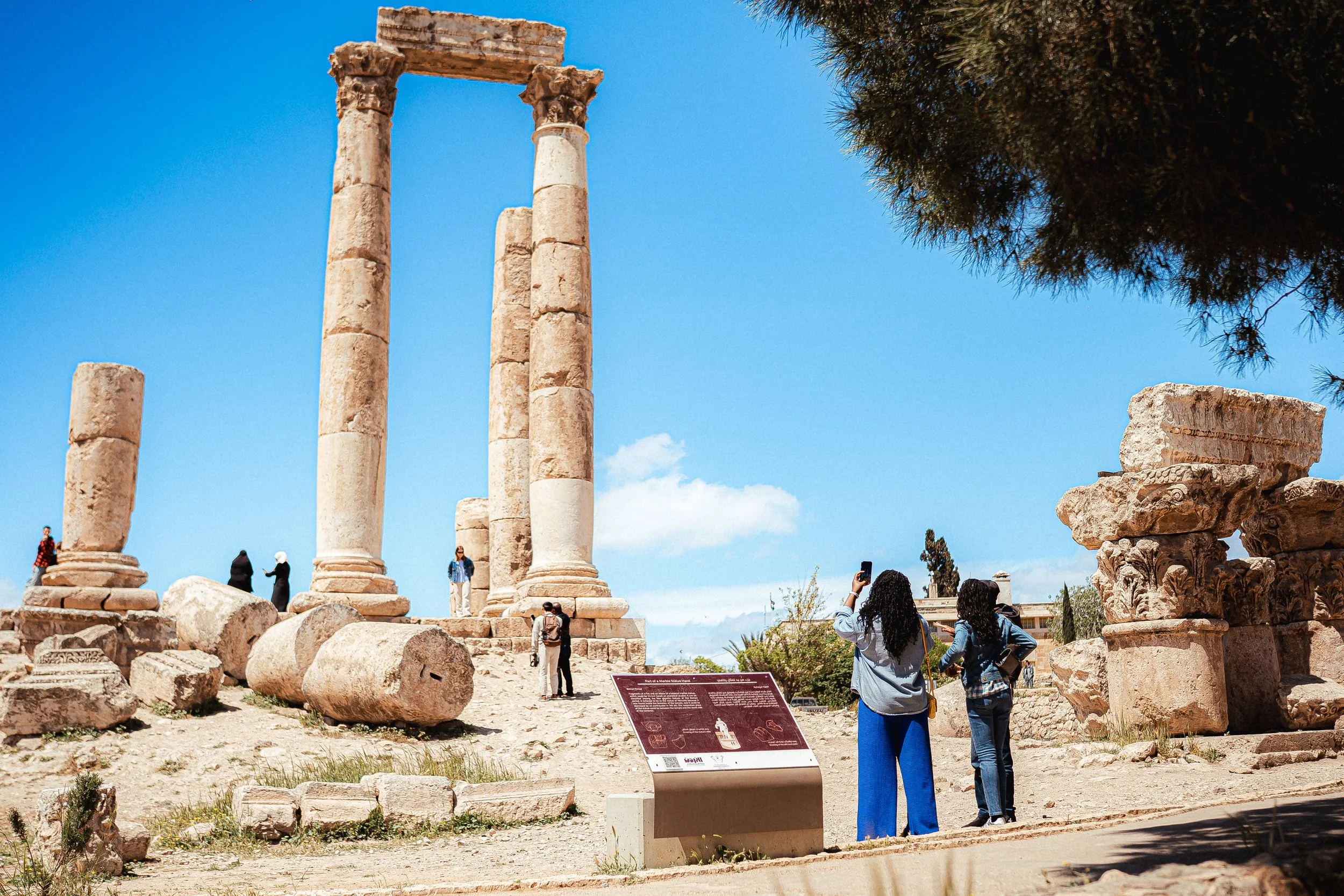Tourists visiting ancient ruins with tall stone columns and scattered stone debris on a sunny day with blue sky