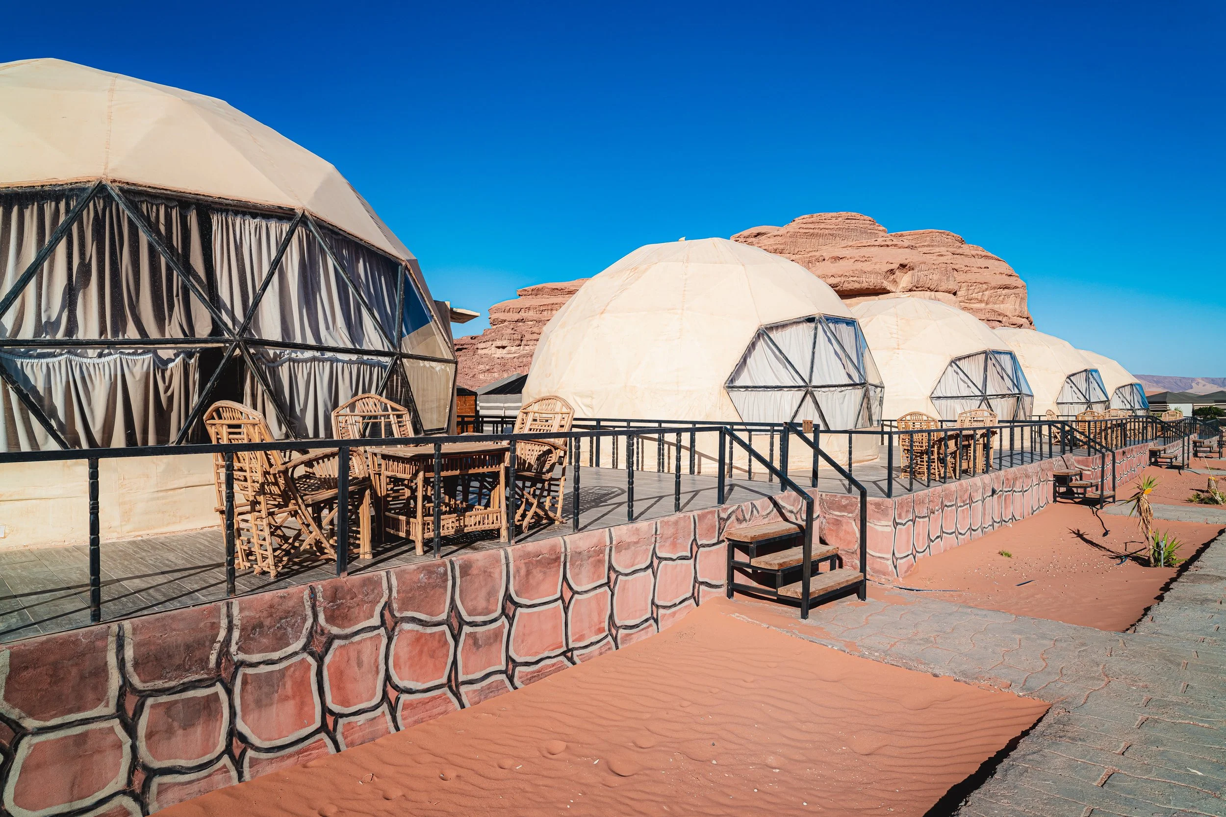Multiple geodesic dome tents on a raised patio with desert landscaping against red rock formations and a clear blue sky.
