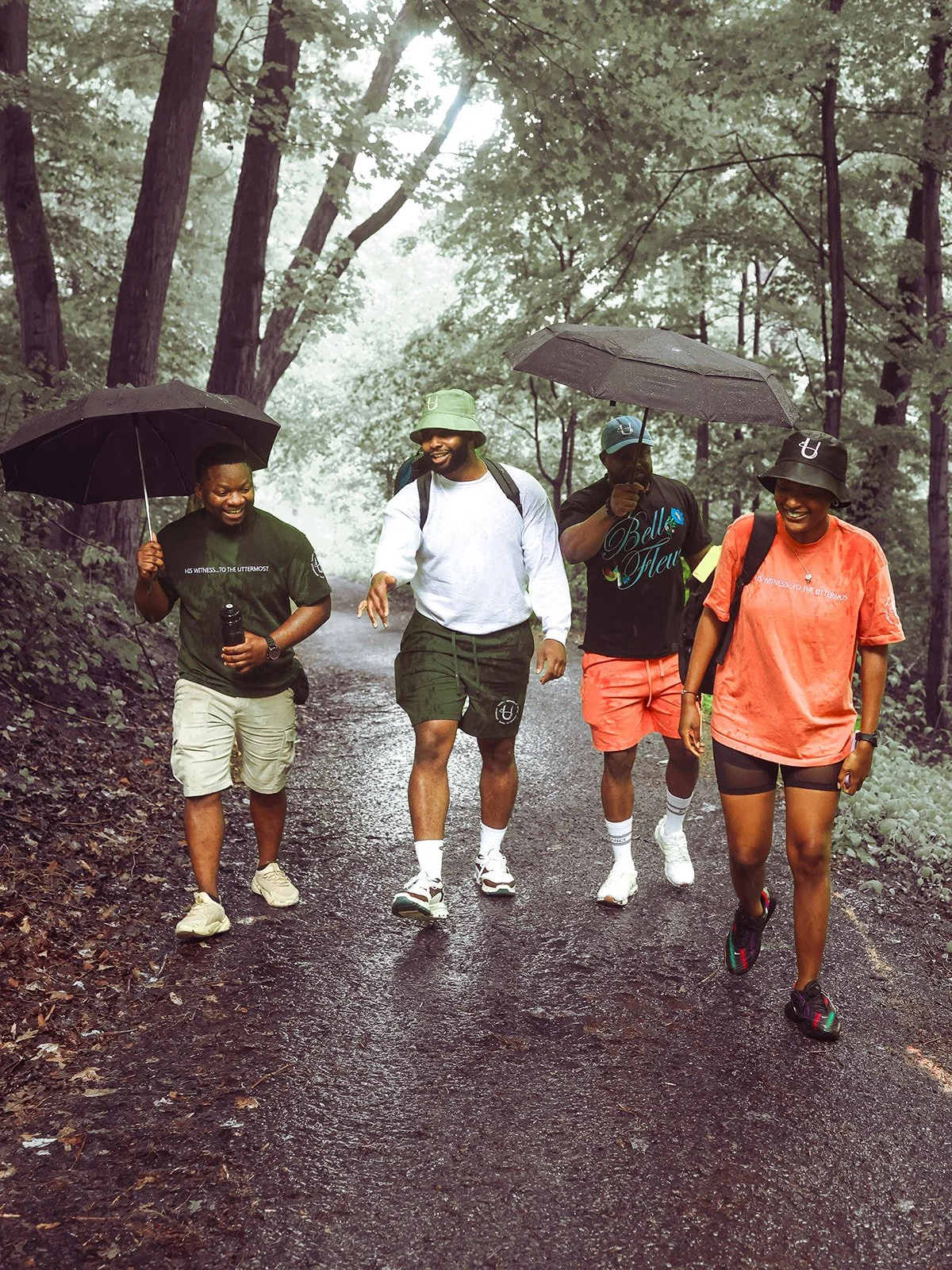 Group of five friends walking with umbrellas on a rainy day in a wooded park, smiling and enjoying the walk.