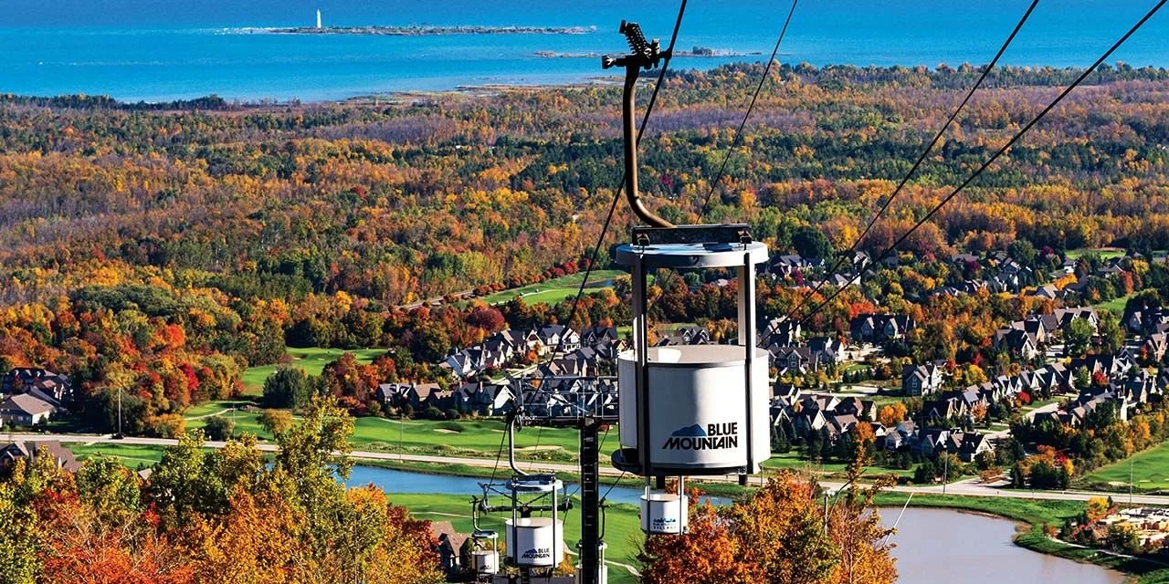 Colorful autumn landscape with a residential neighborhood, golf course, and a lake, seen from a ski lift ascending a mountain in blue mountain village, Ontario, Canada.