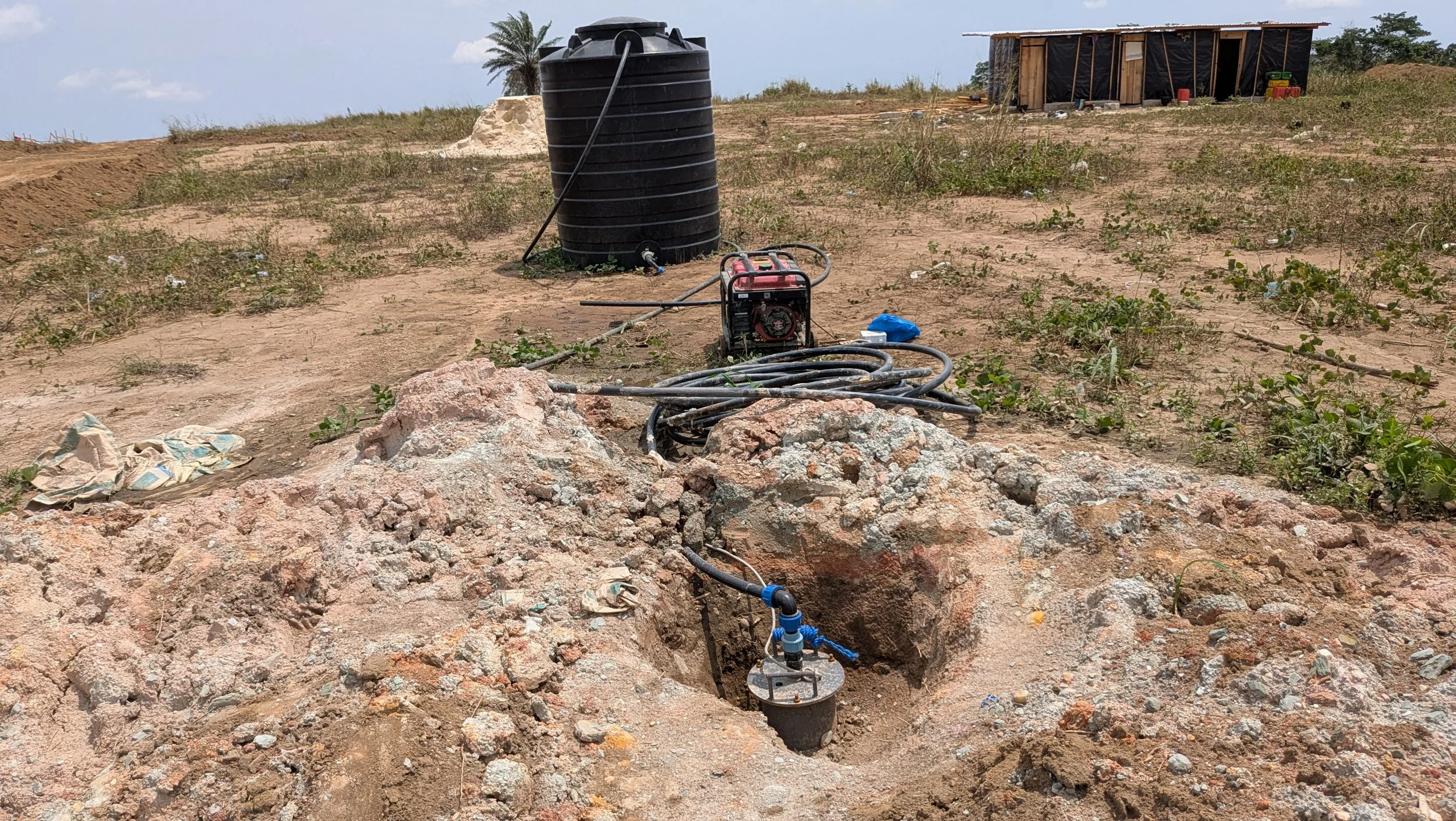 Installation d'un système de pompage d'eau dans un terrain aride avec un réservoir noir, un moteur, et des tuyaux, avec une petite structure en arrière-plan.