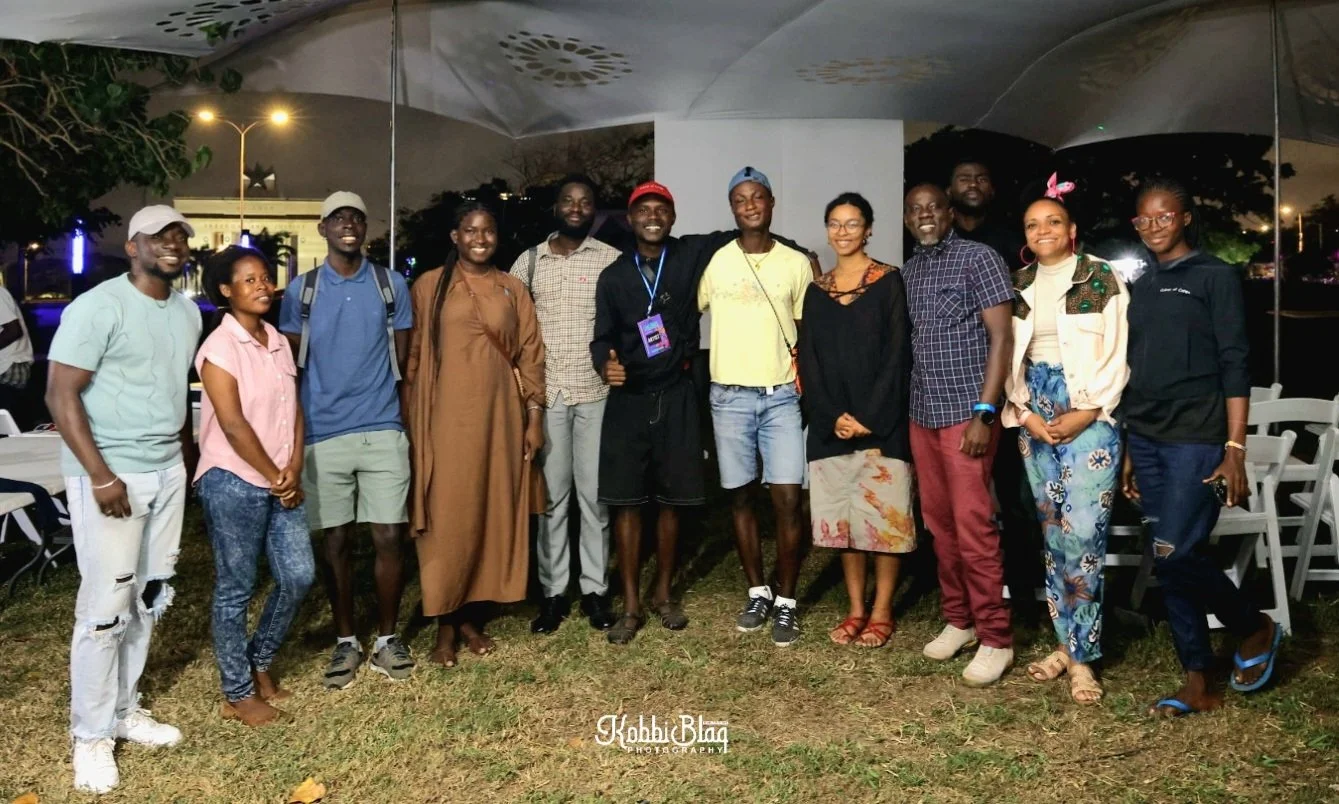 A group of fifteen people standing outdoors at night, smiling for a photo.