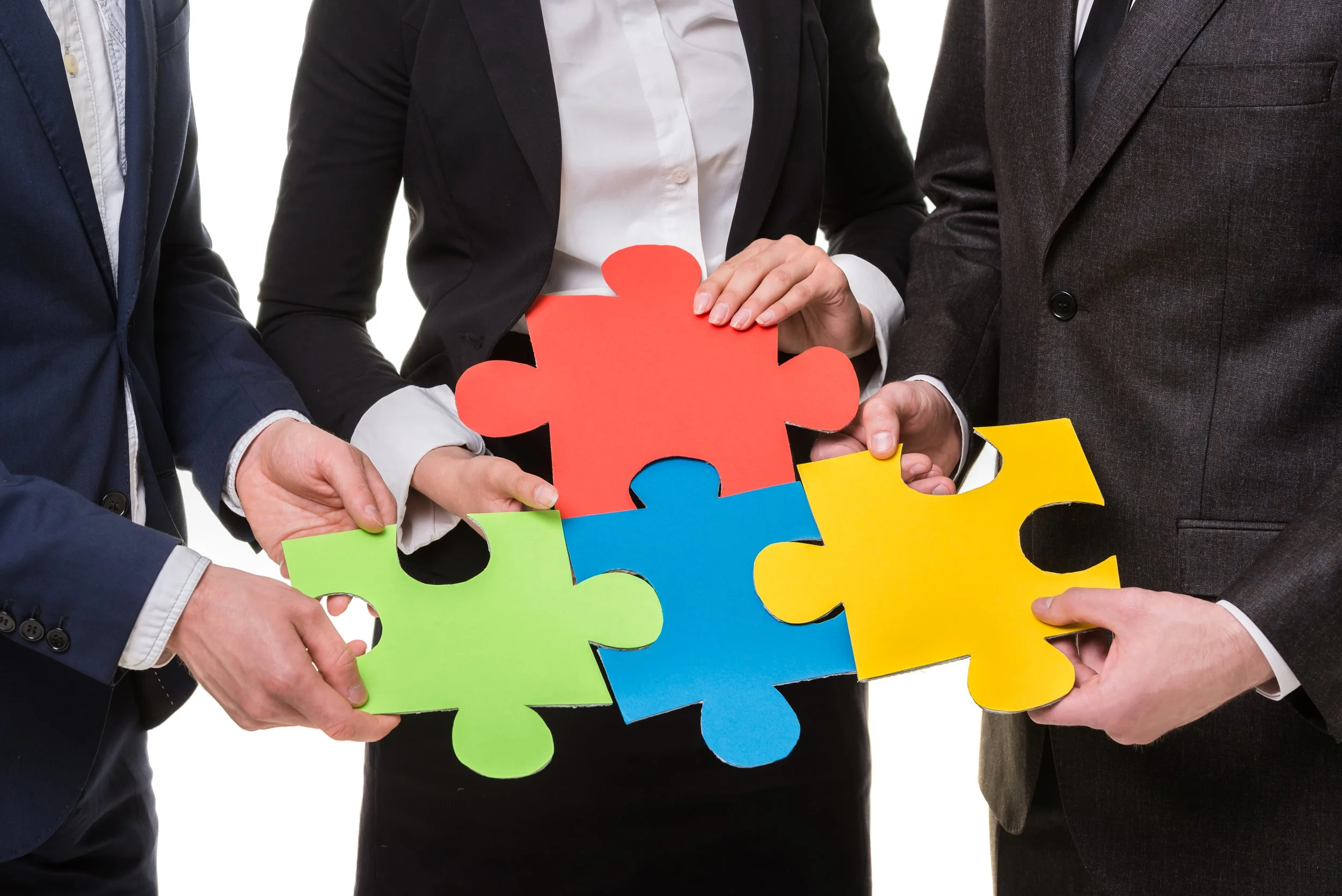 Three businesspeople in suits holding large colorful puzzle pieces together.