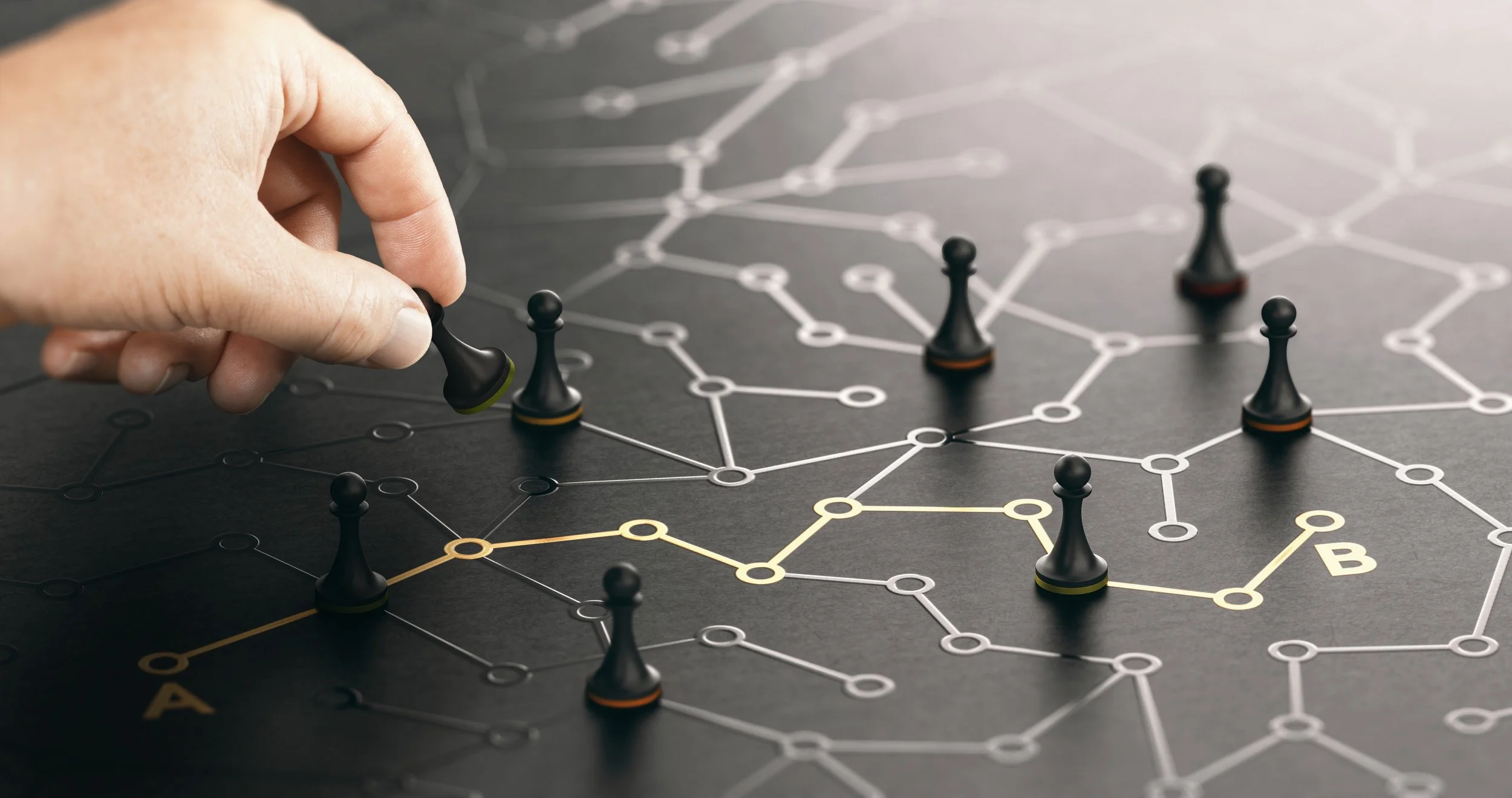 A person's hand moving a black game piece on a strategic board game with interconnected circles and lines forming a network, including a yellow path marked with the letter 'A'.