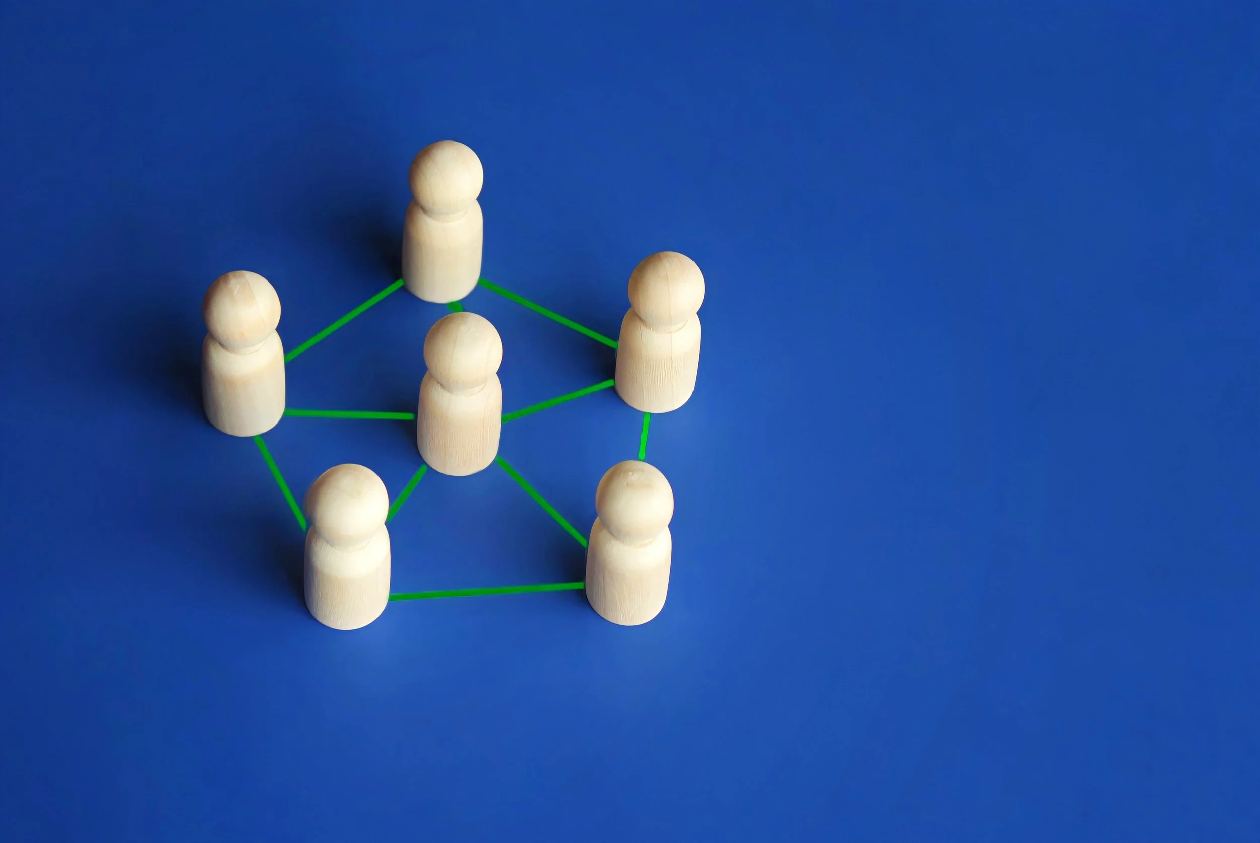 Seven wooden figurines connected by green lines on a blue background, representing a network or social connections.