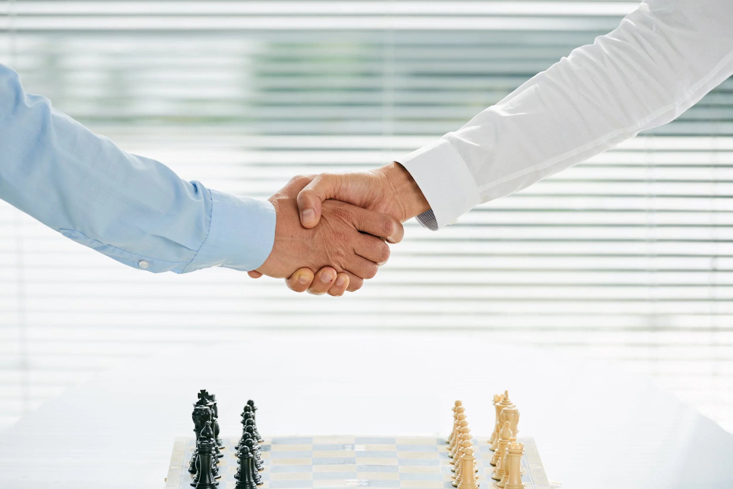 Two people shaking hands over a chessboard.