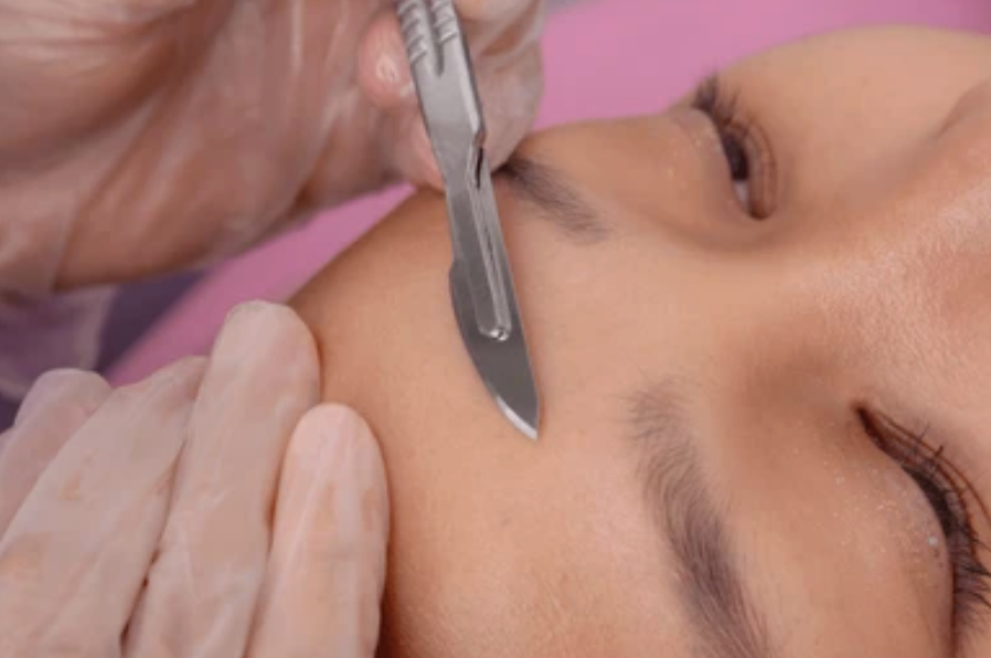 Close-up of a person receiving an eyebrow waxing or shaping treatment, with a technician applying wax or a similar product near the eyebrow area.