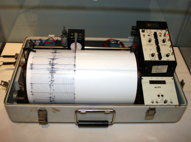 Portable analog seismograph recording seismic activity as jagged ink lines on a rotating paper drum.