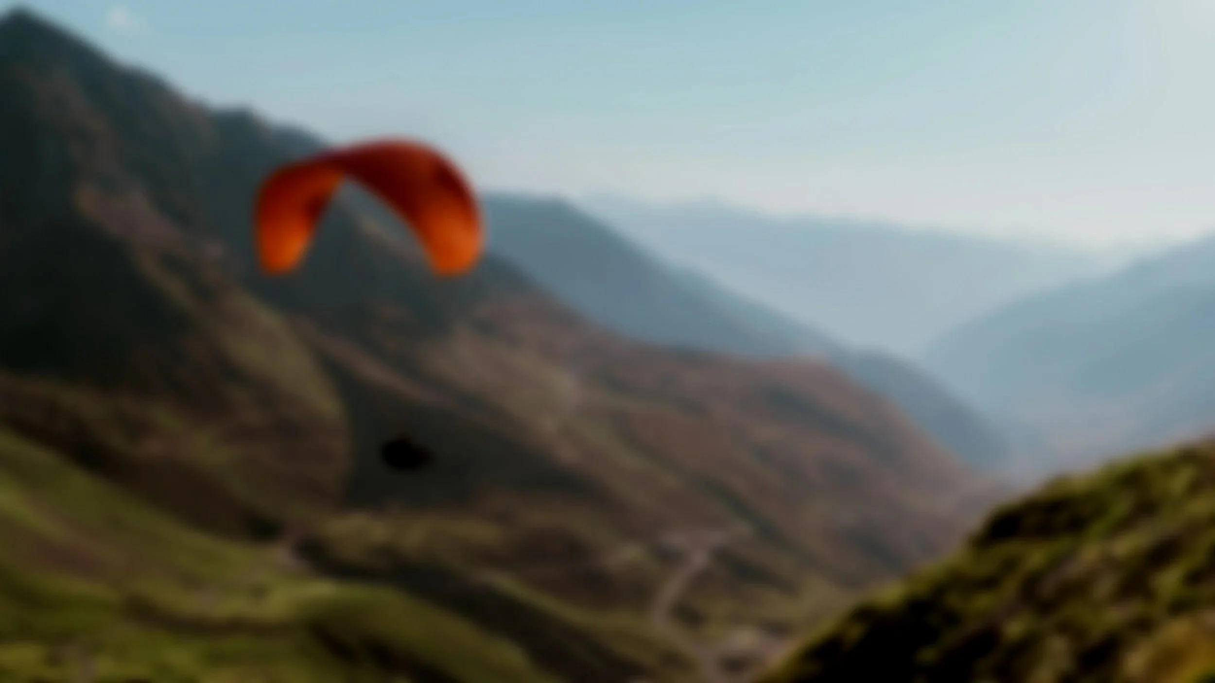 A person flying a parachute over a mountain landscape with valleys and hills.