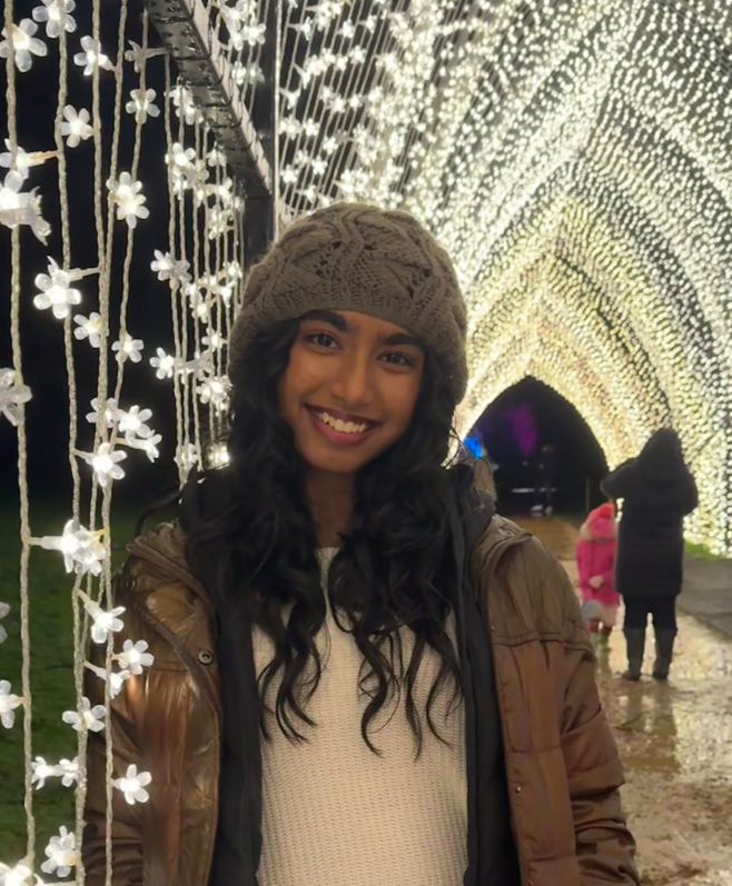A woman smiling at a holiday light display with a tunnel of illuminated white flowers.