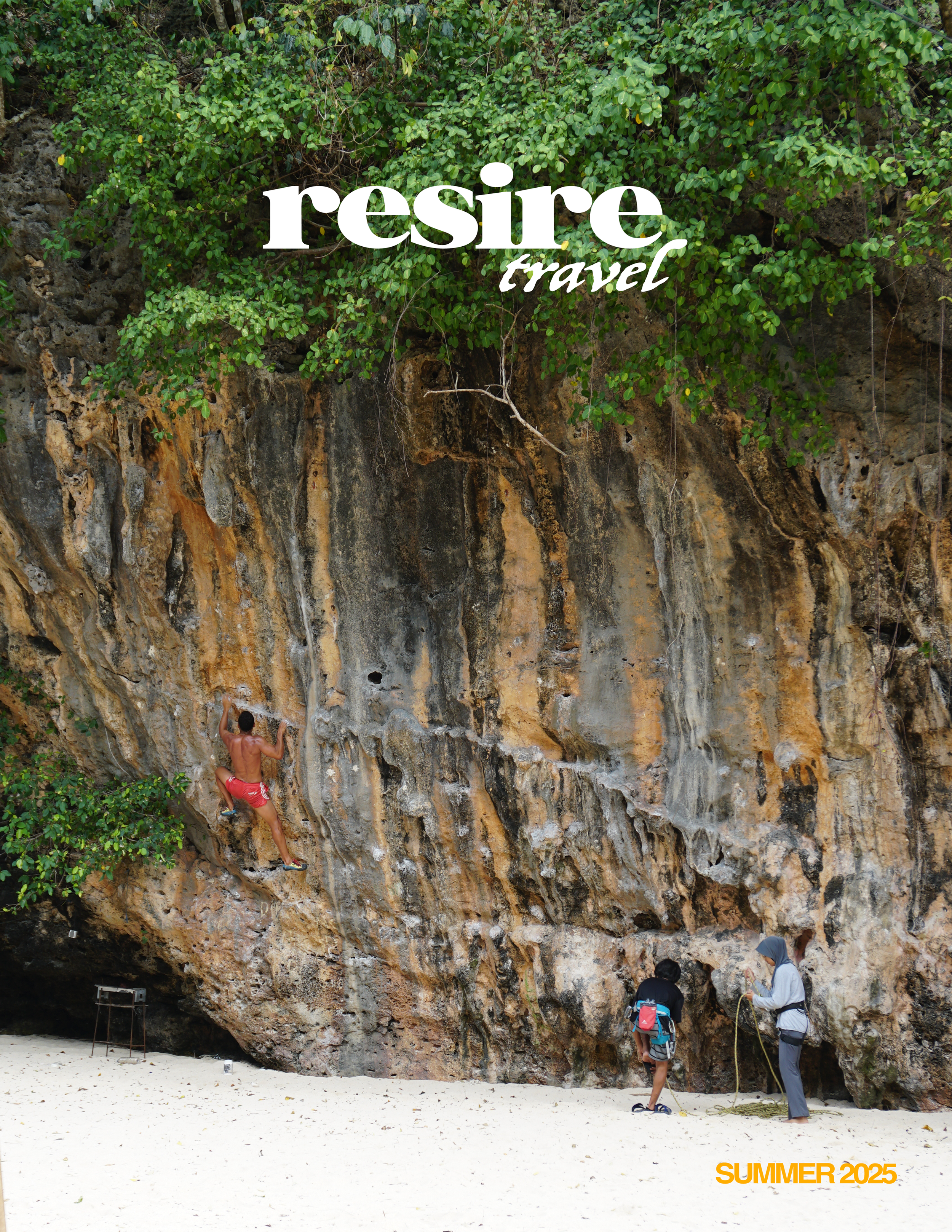 A person rock climbing on a cliff by the beach while two others supervise below, with green foliage above and sandy ground at the bottom, promoting travel and summer activities for 2025.