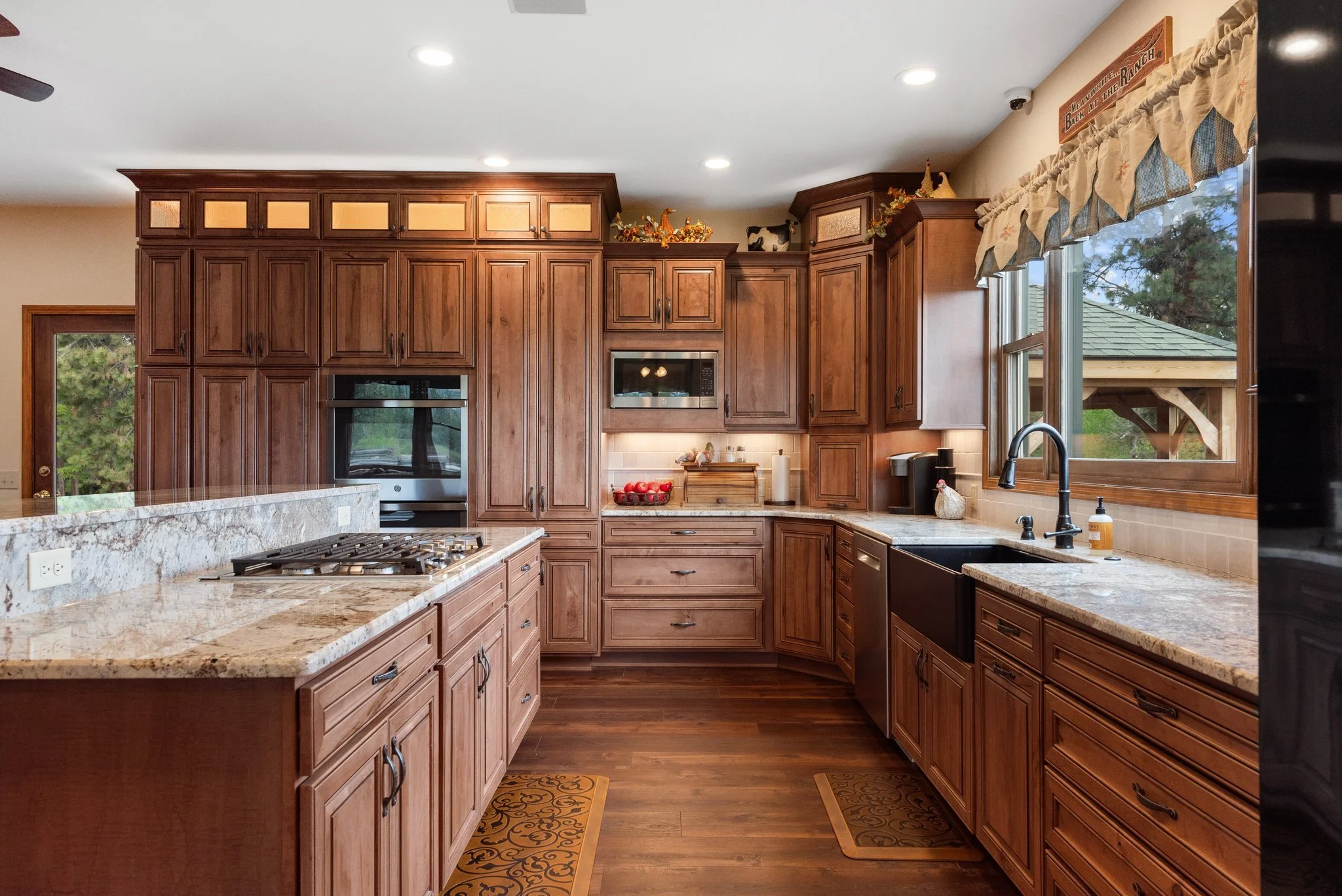 Kitchen with wooden cabinets, granite countertops, a window over the sink, and a hanging sign that reads 'Memories Love the Best at the Ranch.'