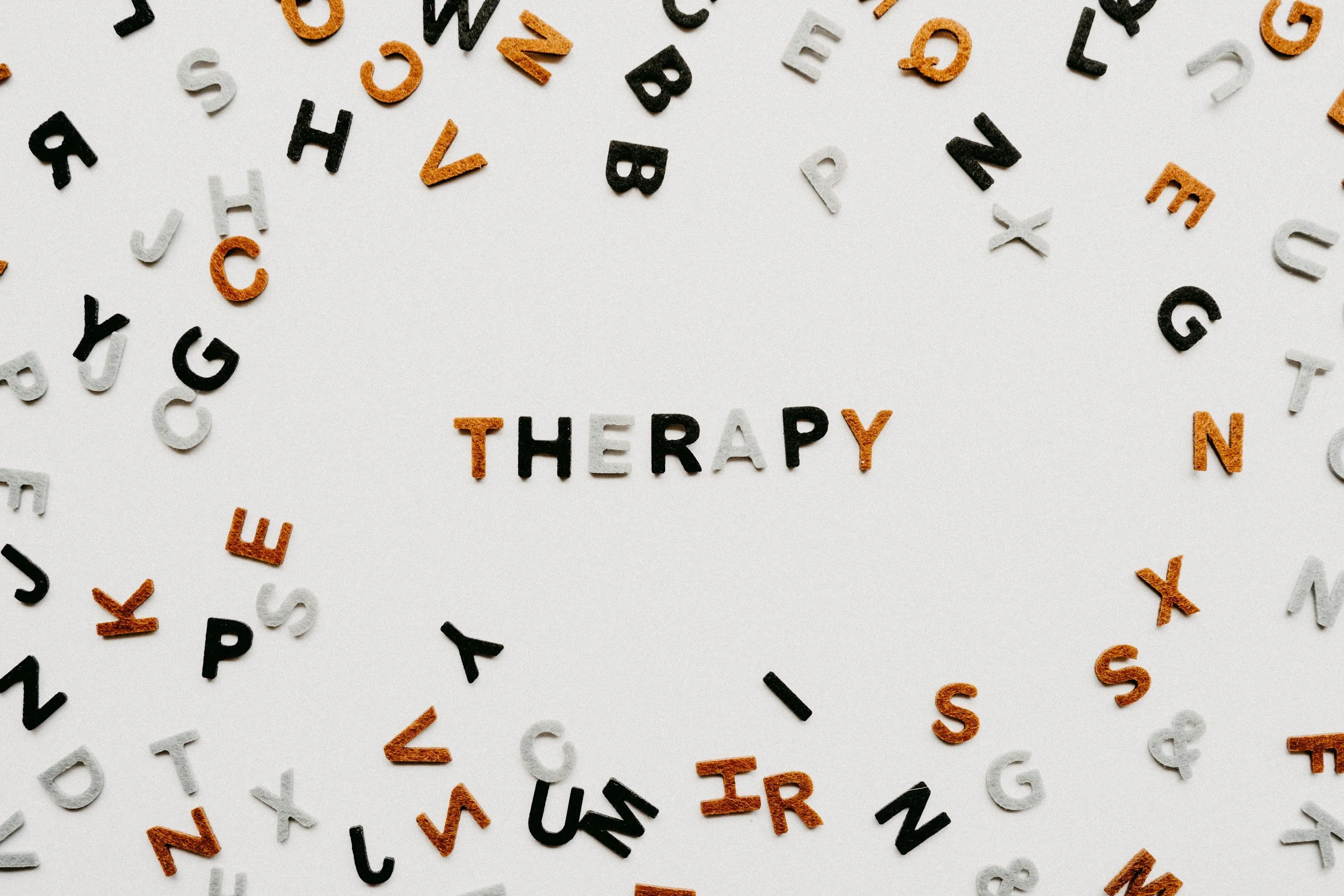 Colorful scattered letter tiles with the word "THERAPY" spelled in the center.