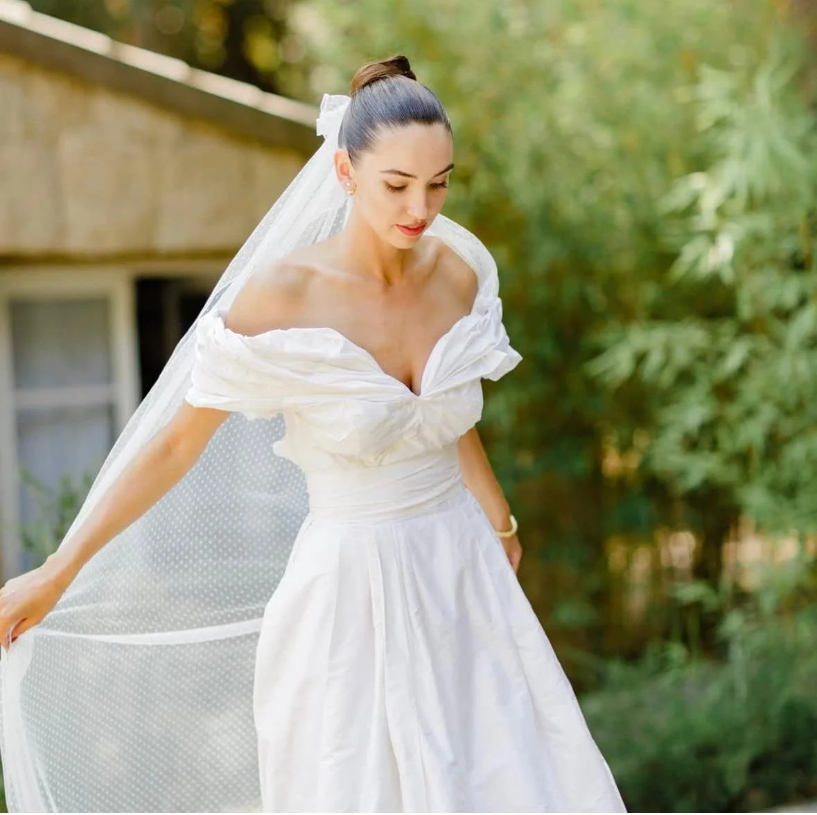 Jeune femme en robe de mariage blanche avec un voile, dans un jardin.