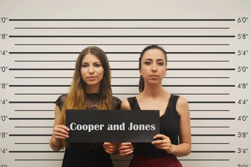 Two women standing in front of a height measurement wall holding a sign that reads "Cooper and Jones".