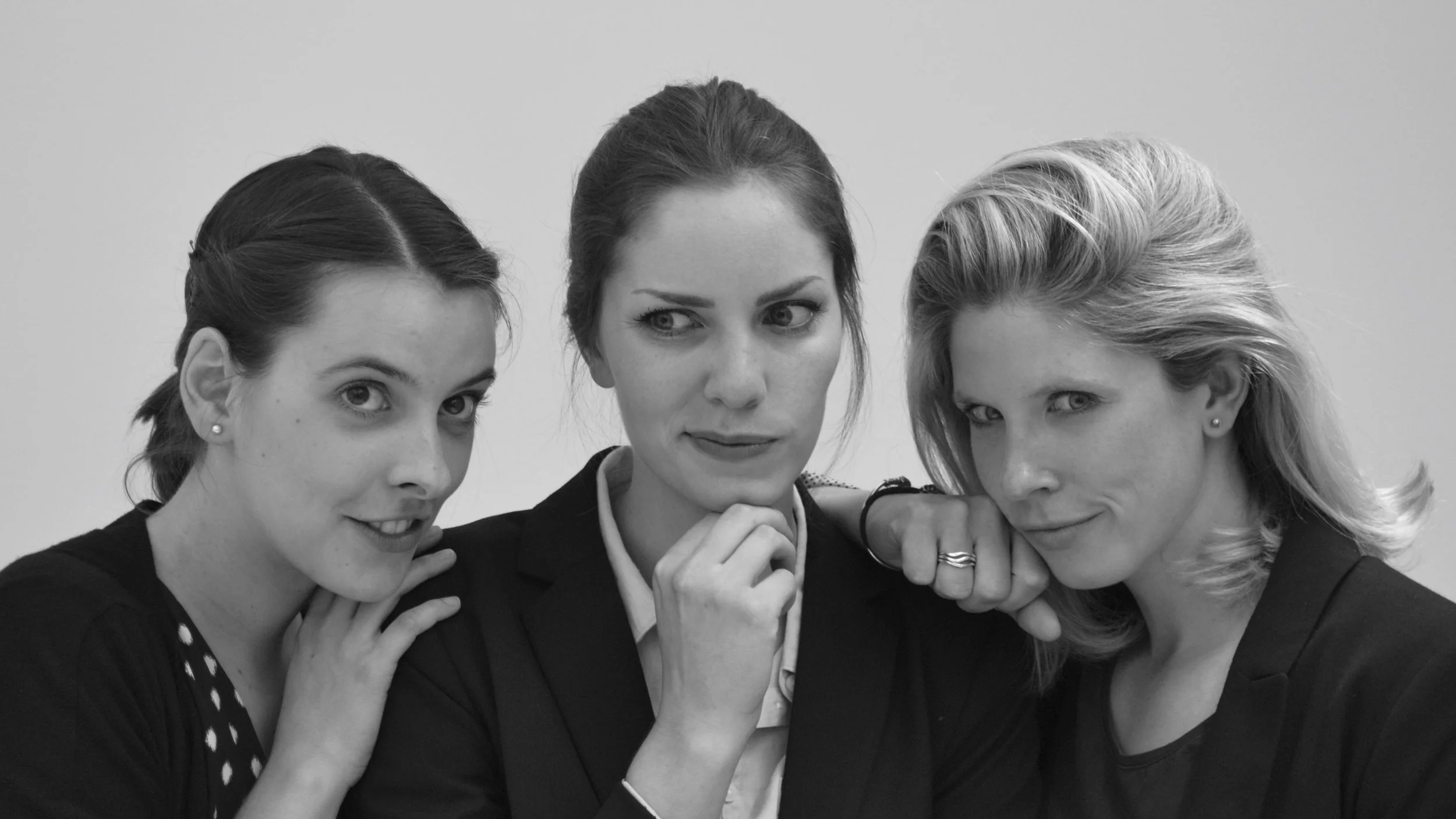 Three women dressed in business attire posing together in black and white photo.