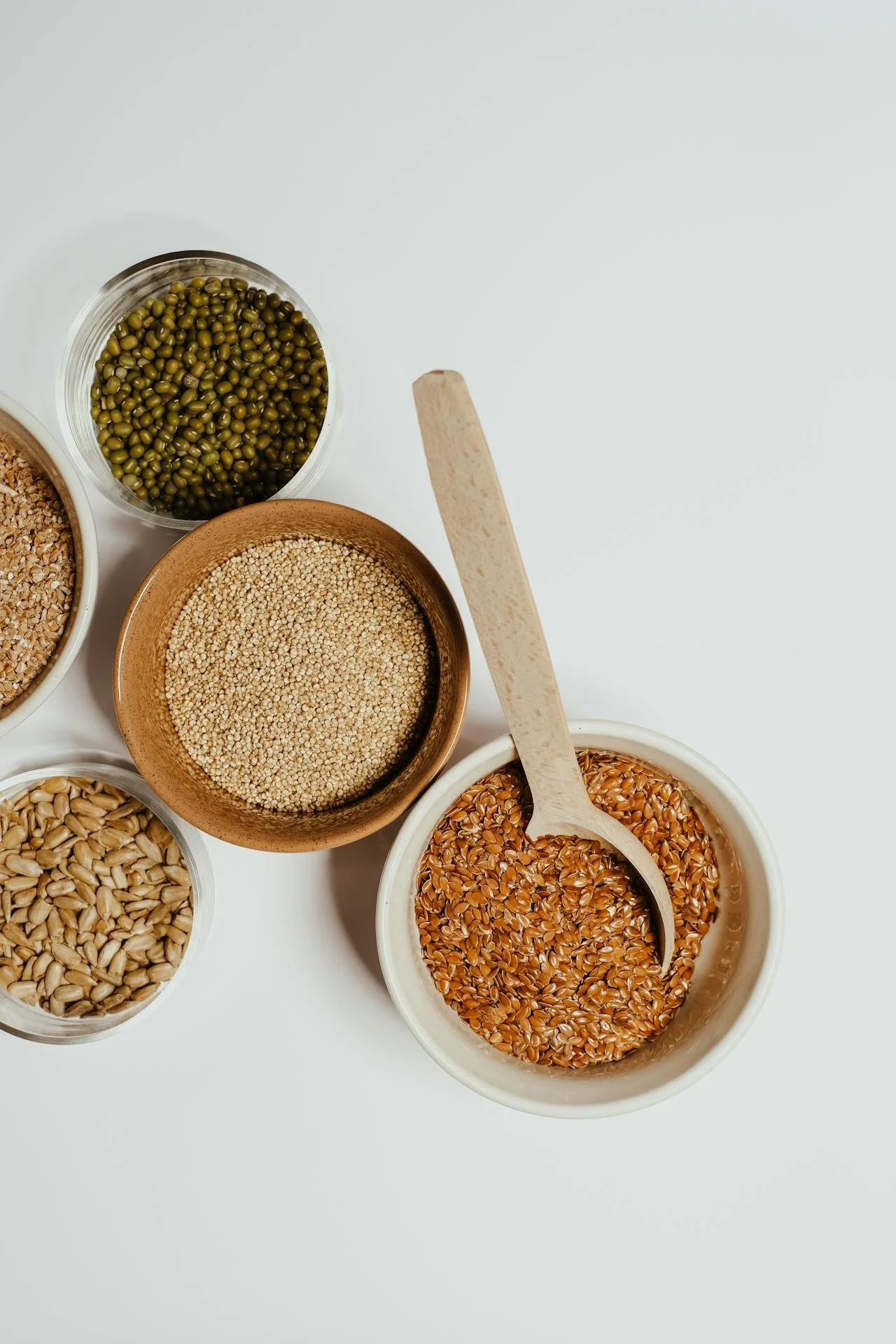 Various bowls containing grains, seeds, and lentils on a white surface.