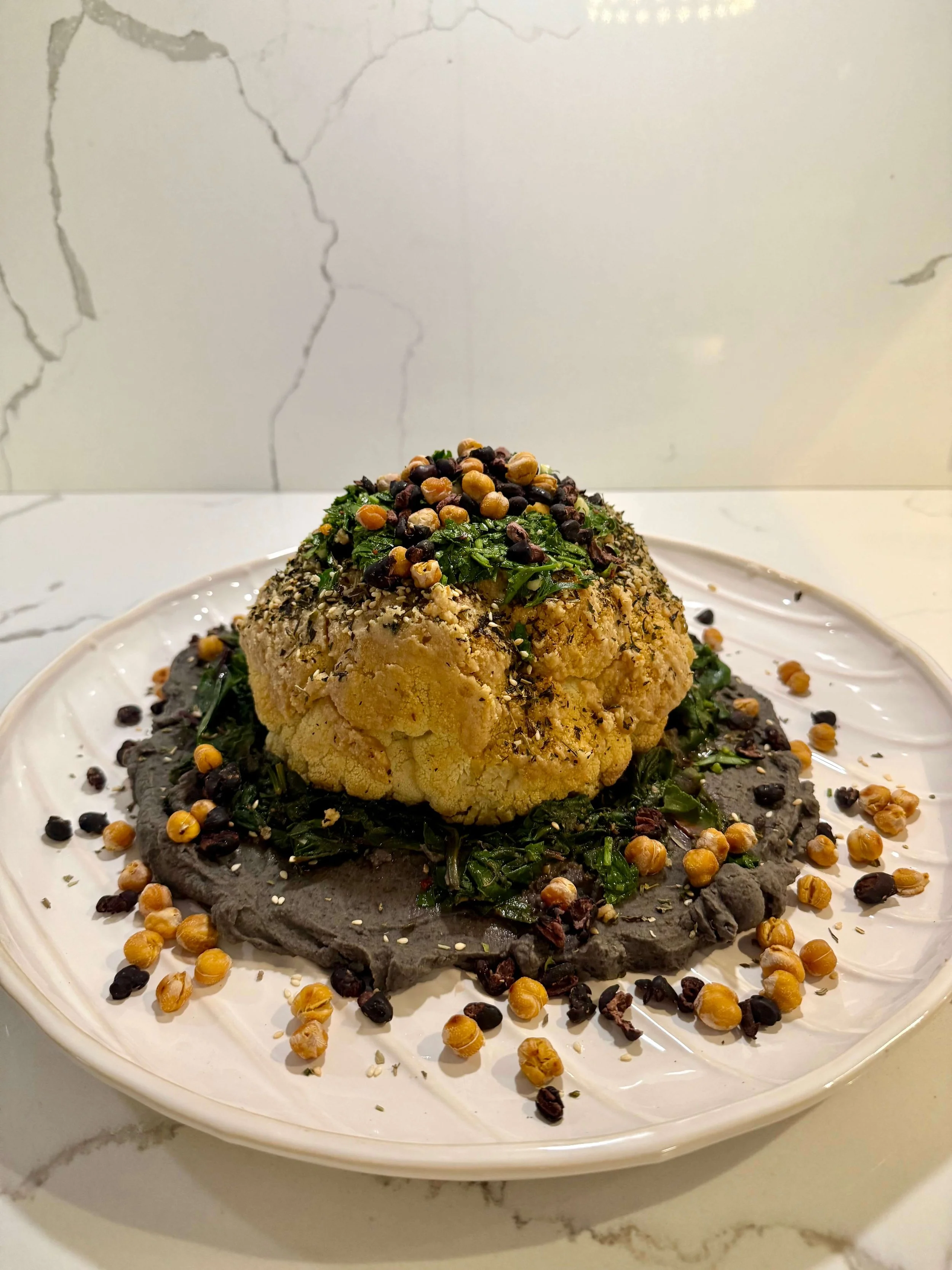 a whole roasted cauliflower with black bean dip and crunchy beans