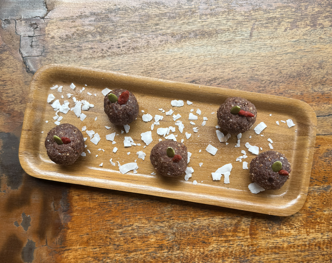 Bean-powered energy bites arranged on a wooden serving tray, topped with seeds and coconut flakes.