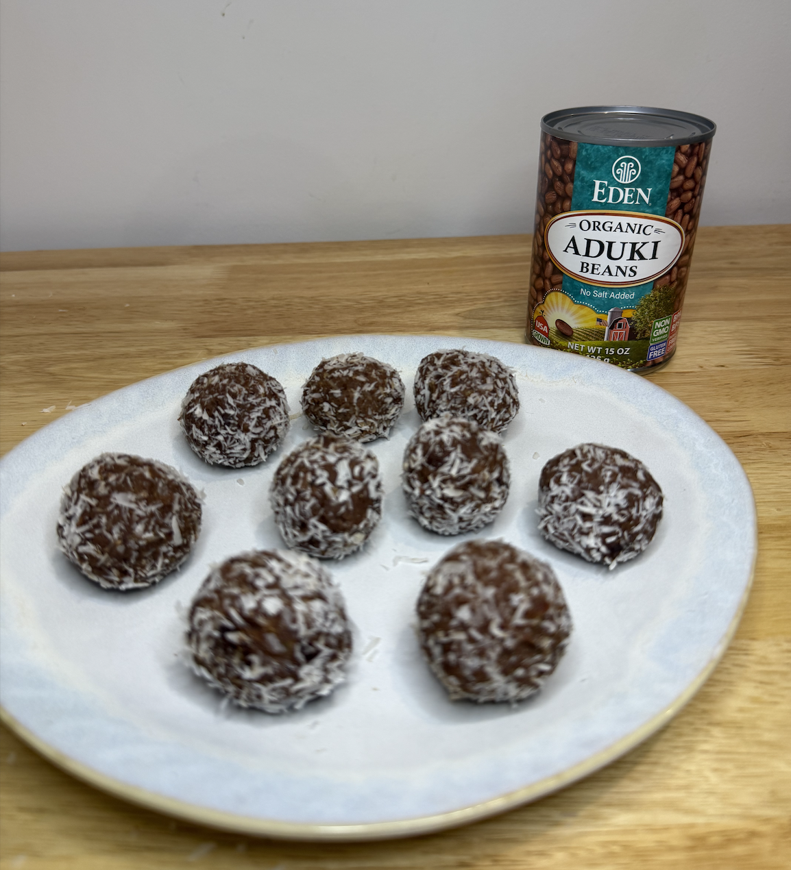 Bean-powered energy bites rolled in shredded coconut on a ceramic plate, with a can of organic adzuki beans in the background