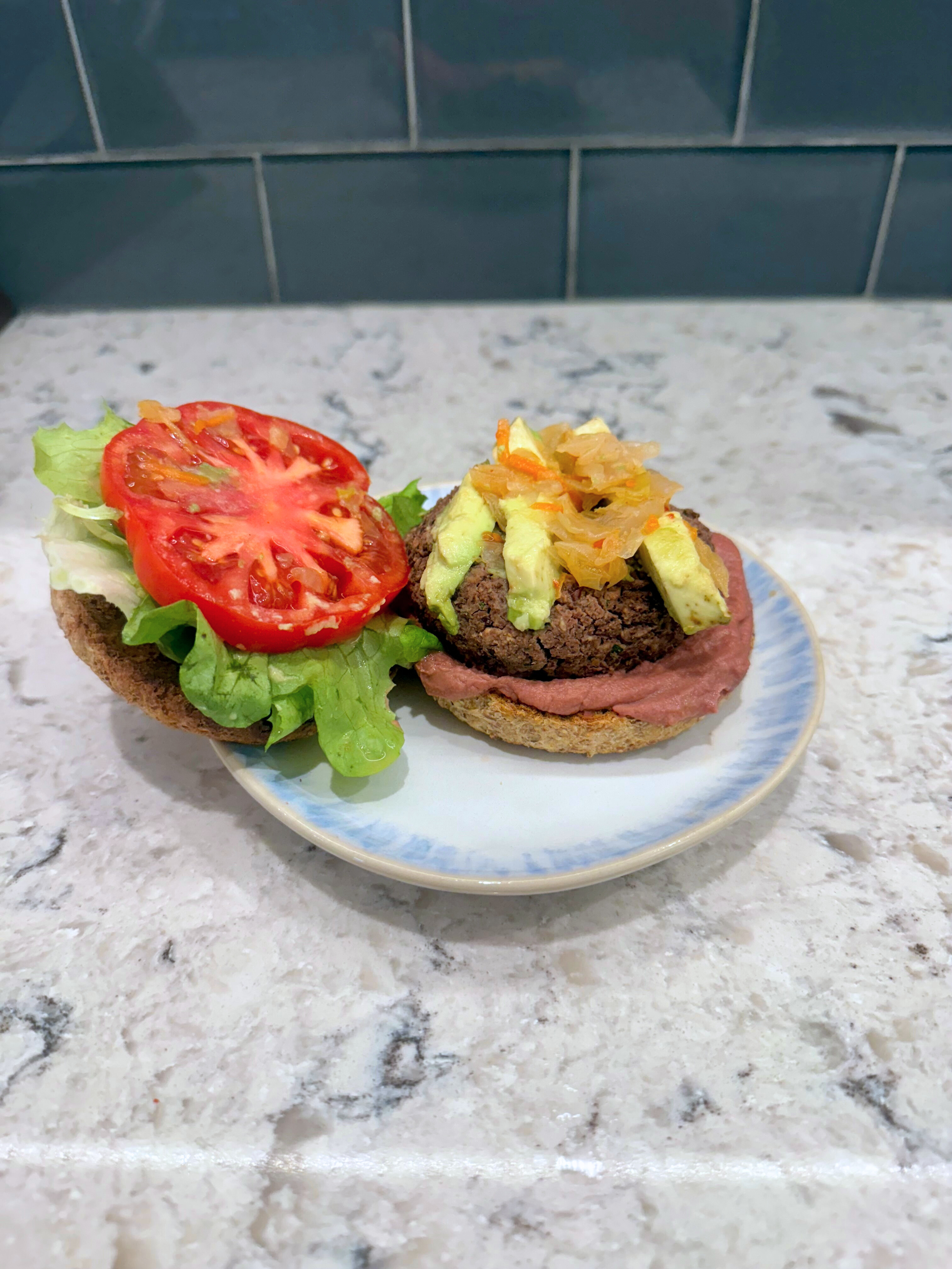 Vegan black bean burger topped with avocado, sauerkraut, lettuce, and tomato on a bun.