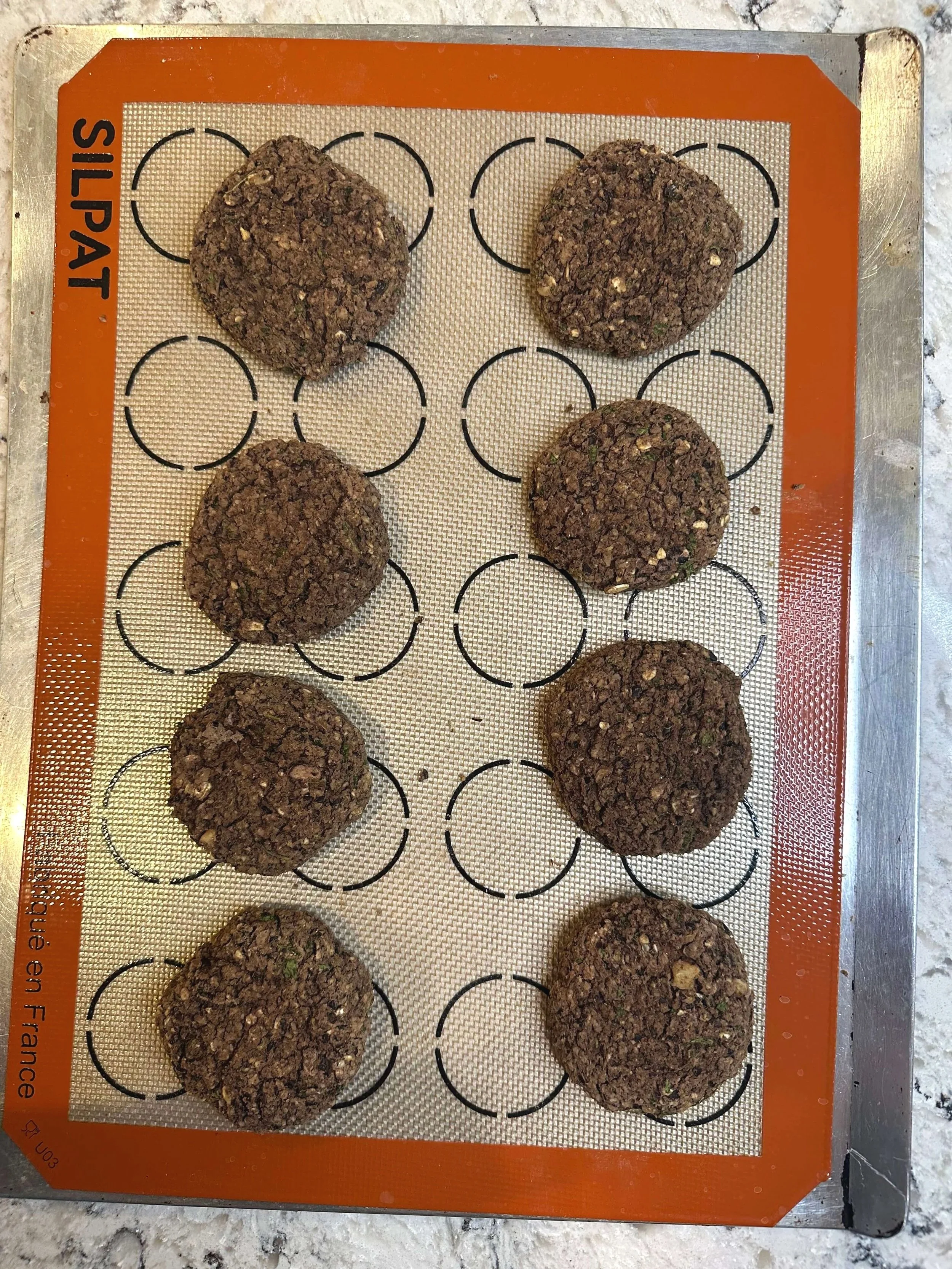 Black bean burger patties shaped and baked on a silicone baking mat, showing before and after cooking texture.