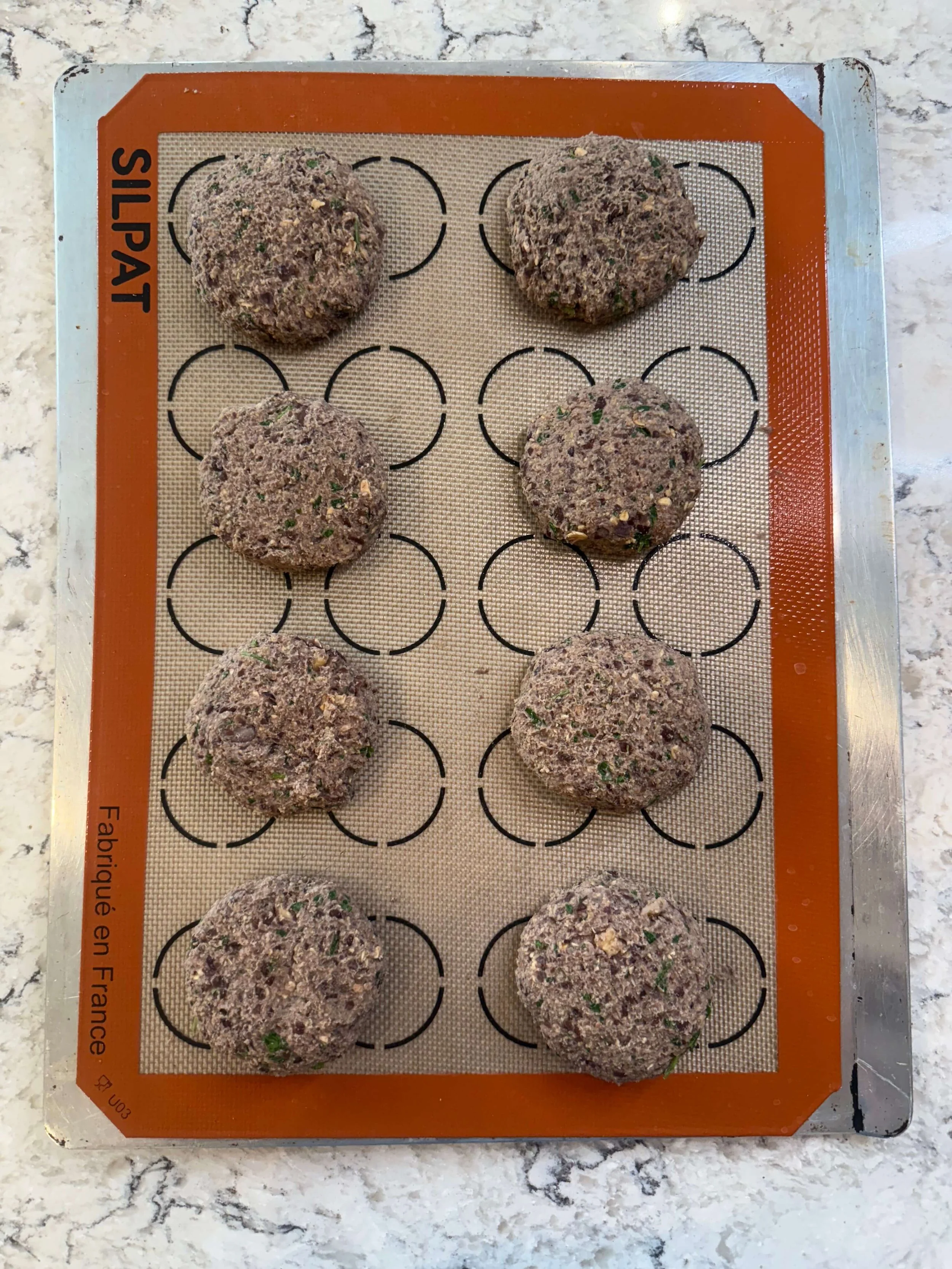 Black bean burger patties shaped and baked on a silicone baking mat, showing before and after cooking texture.