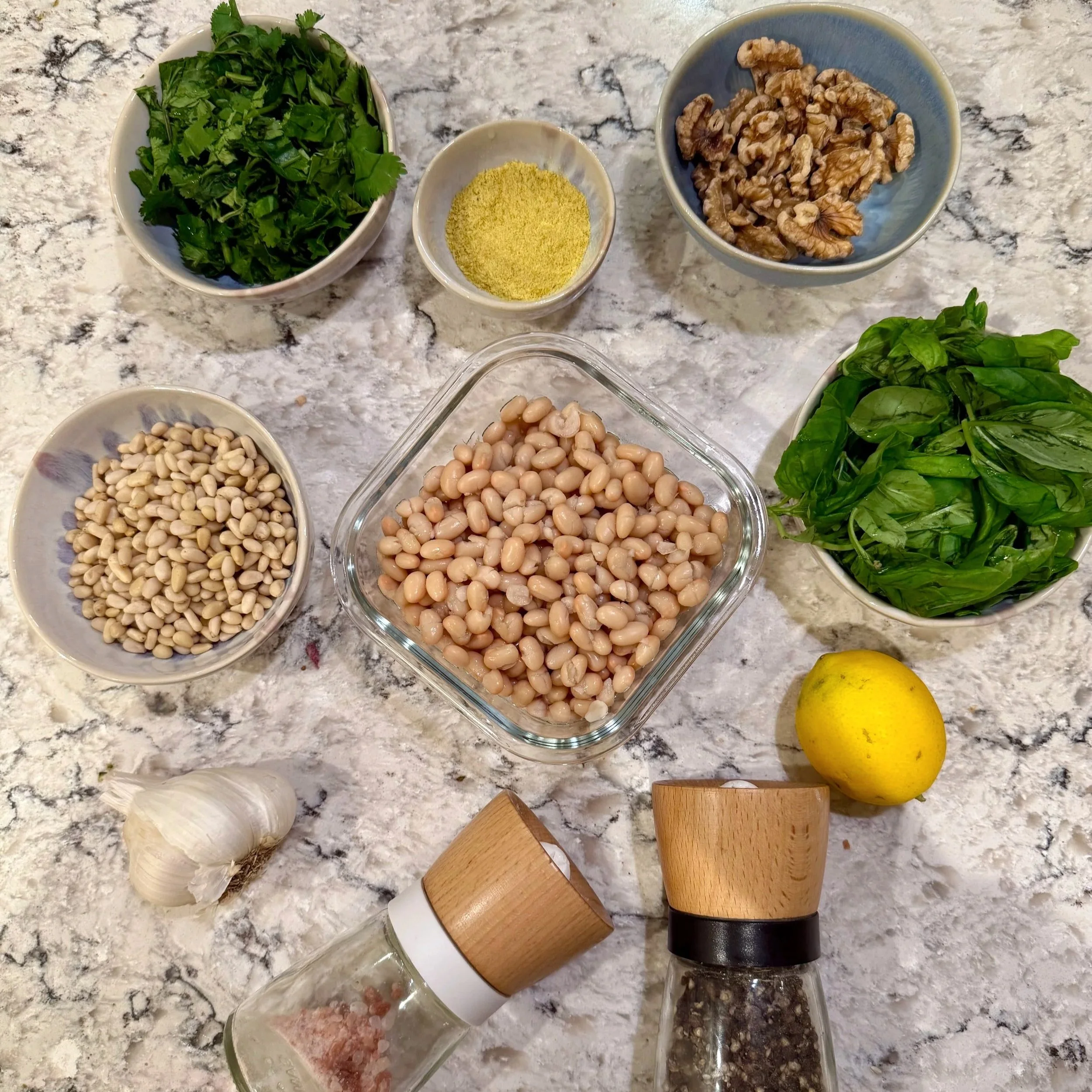 Ingredients for vegan white bean pesto including navy beans, basil, parsley, walnuts, pine nuts, garlic, and lemon
