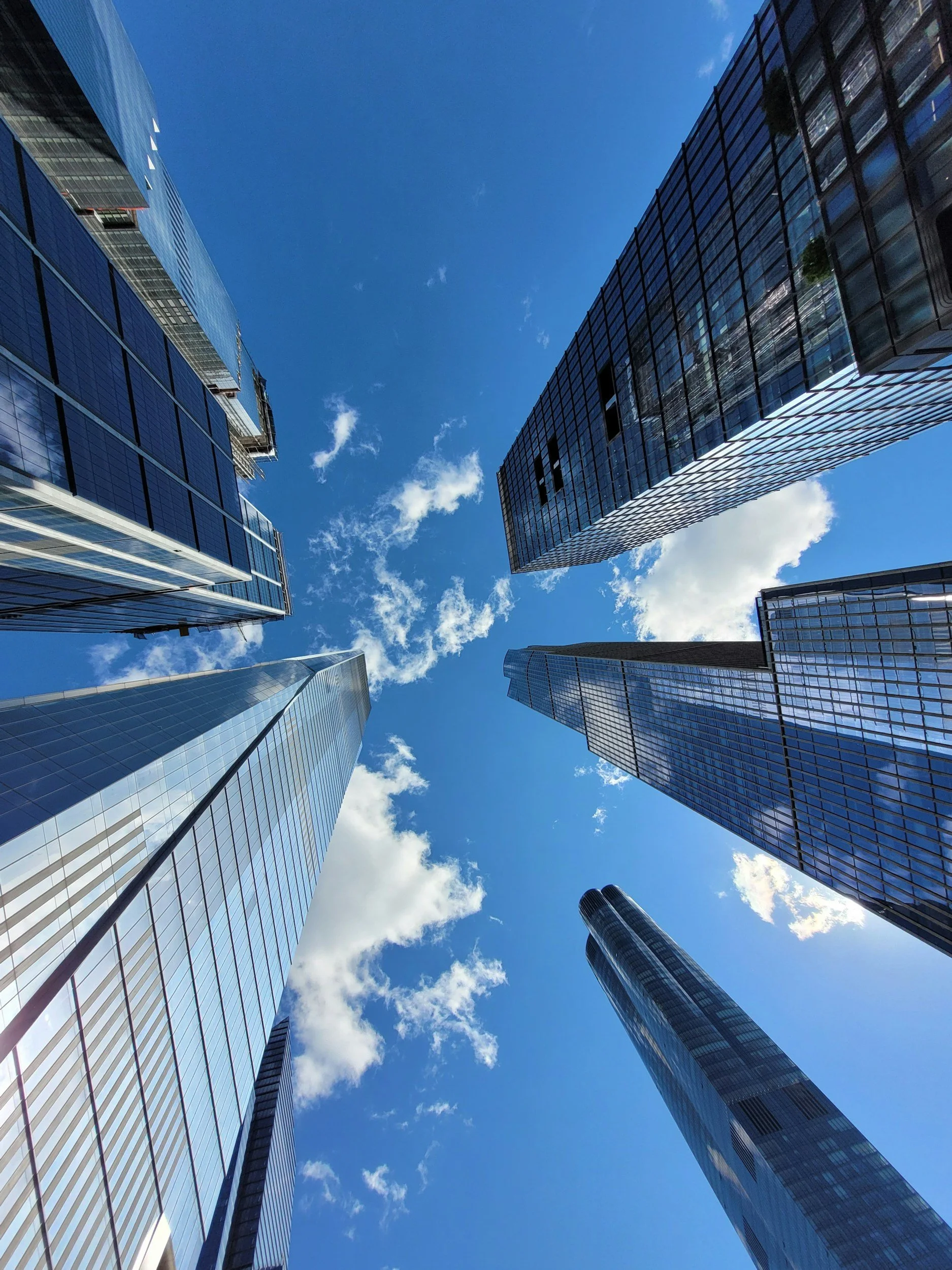 Looking upward at modern glass skyscrapers against a blue sky with some clouds.