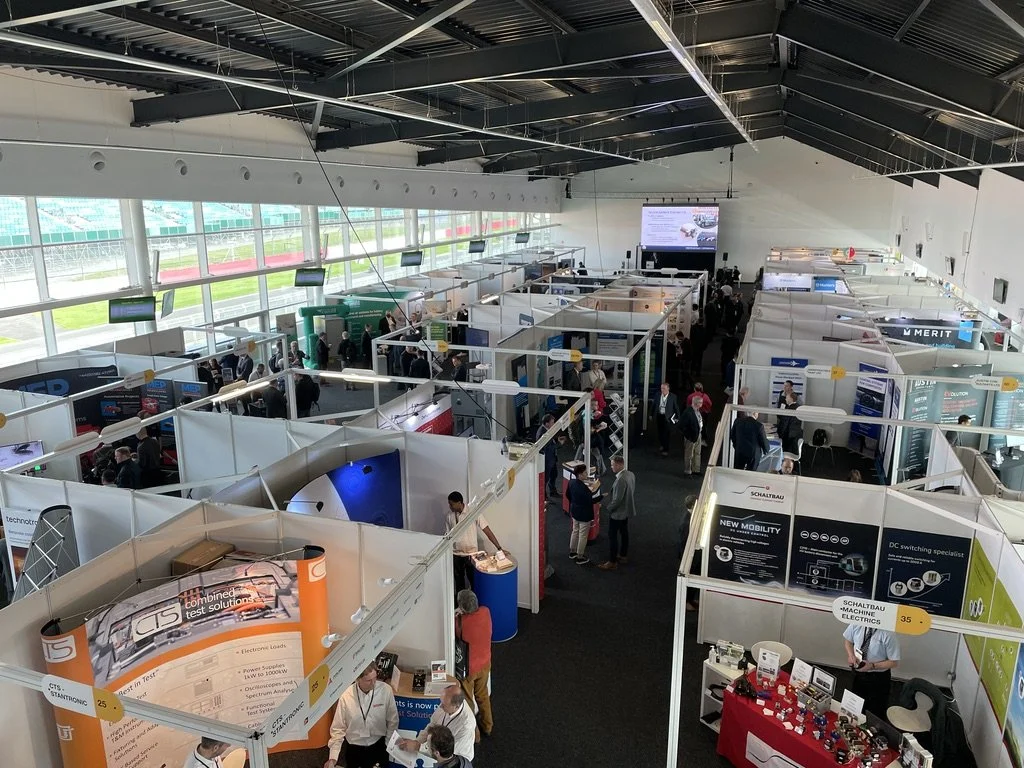 A large conference or trade show with numerous booths and attendees inside a spacious hall.