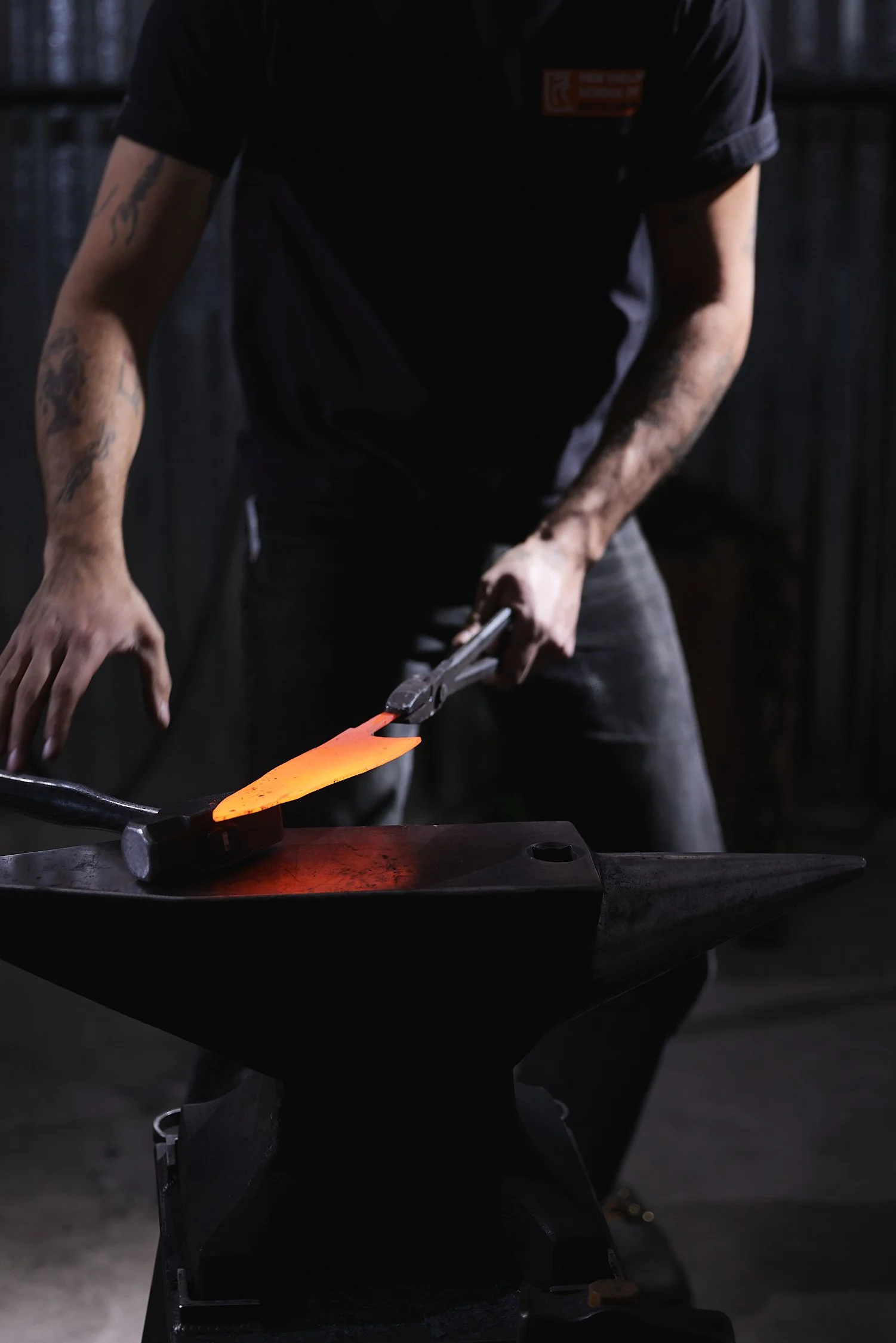 A blacksmith working on a glowing piece of metal on an anvil outdoors at night.