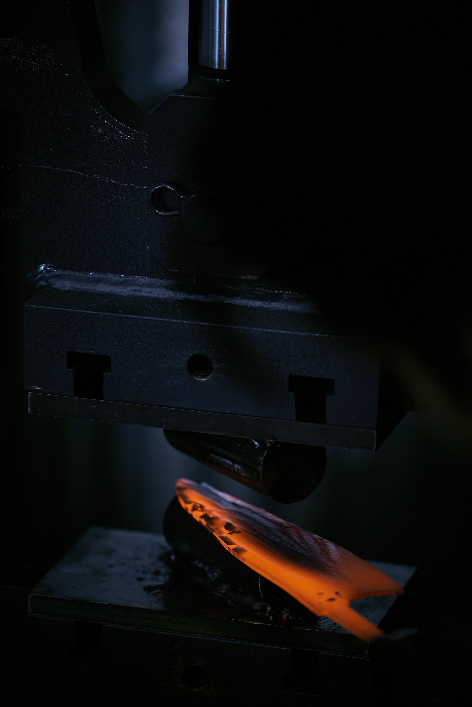 A blacksmith forging a metal piece with glowing orange hot metal heated in a forge or furnace.