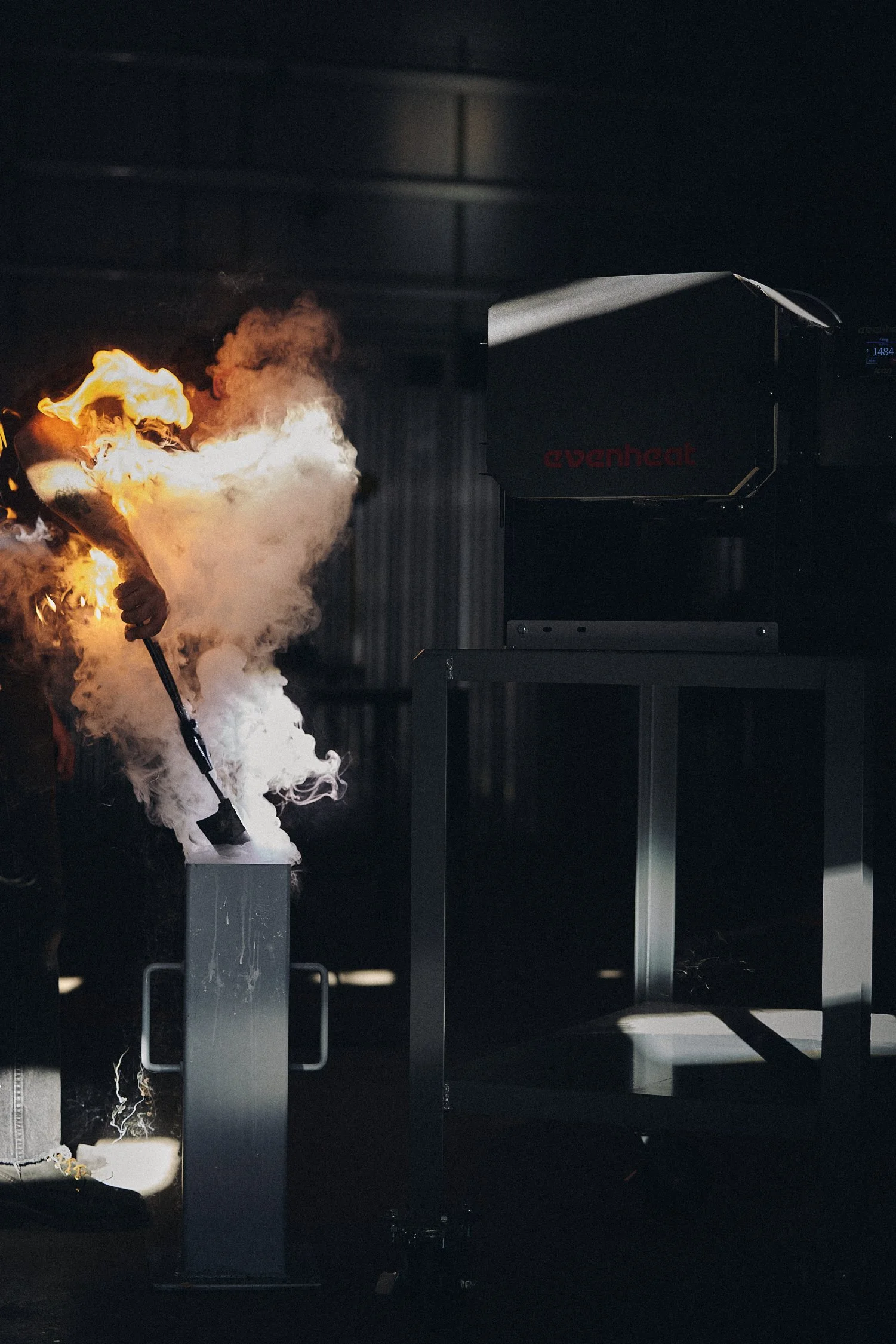 Person igniting a fire during a demonstration, with flames and smoke, in a dark indoor setting.
