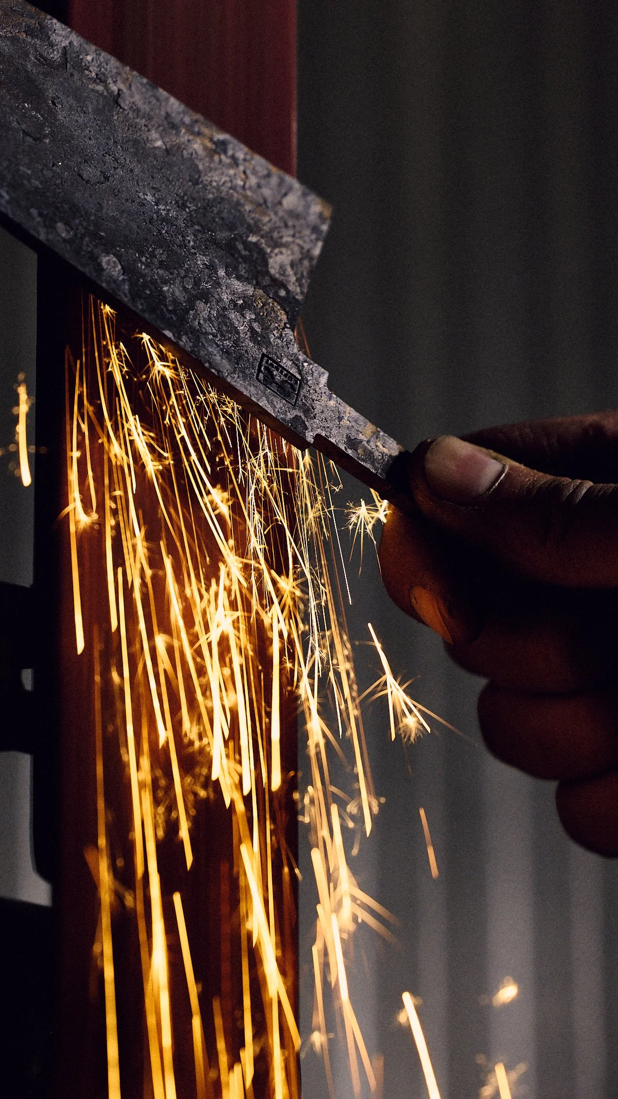 Close-up of a craftsman's hand grinding a piece of metal, sparks flying in the air.