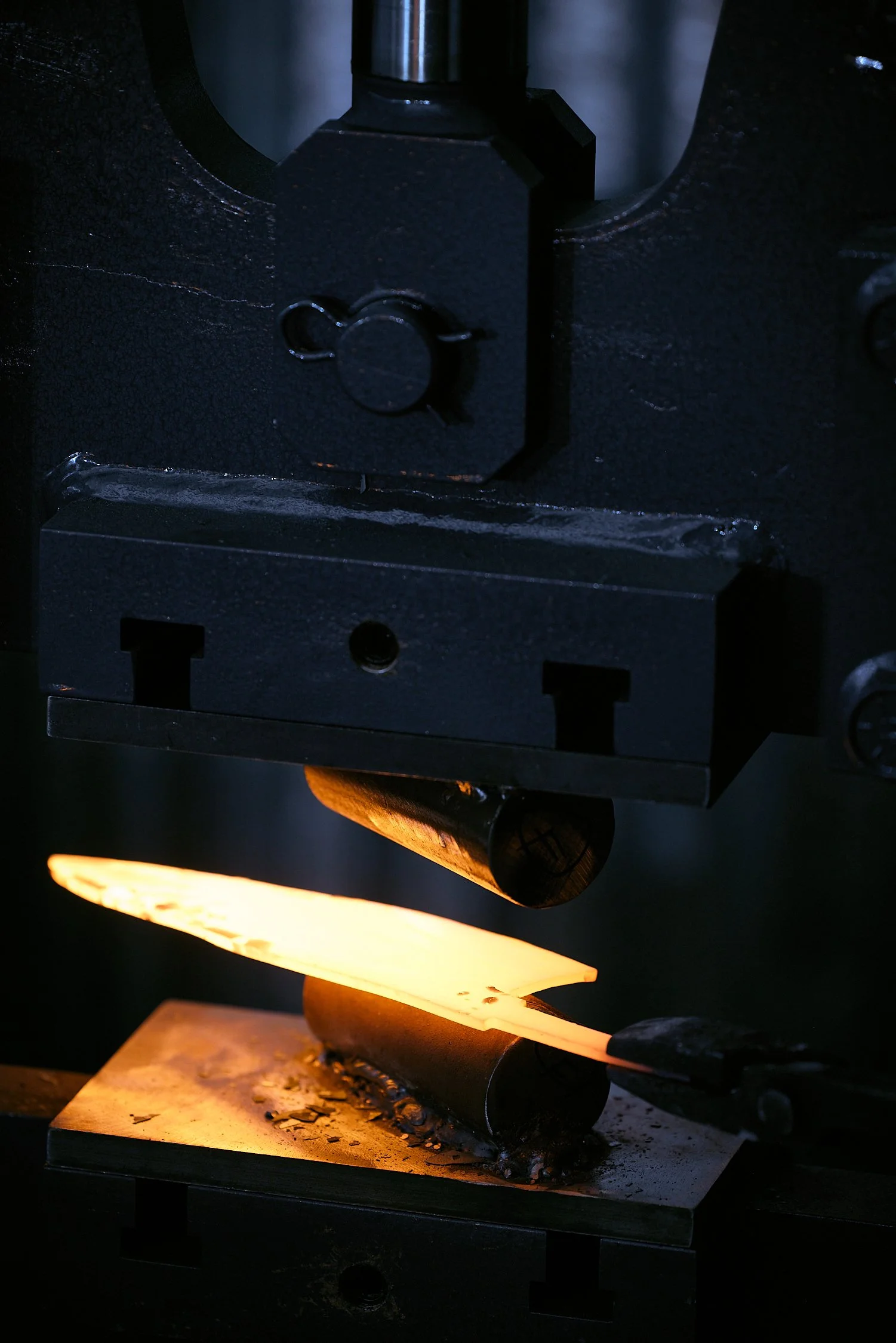A craftsman forging a glowing metal piece using a hydraulic press in a workshop.