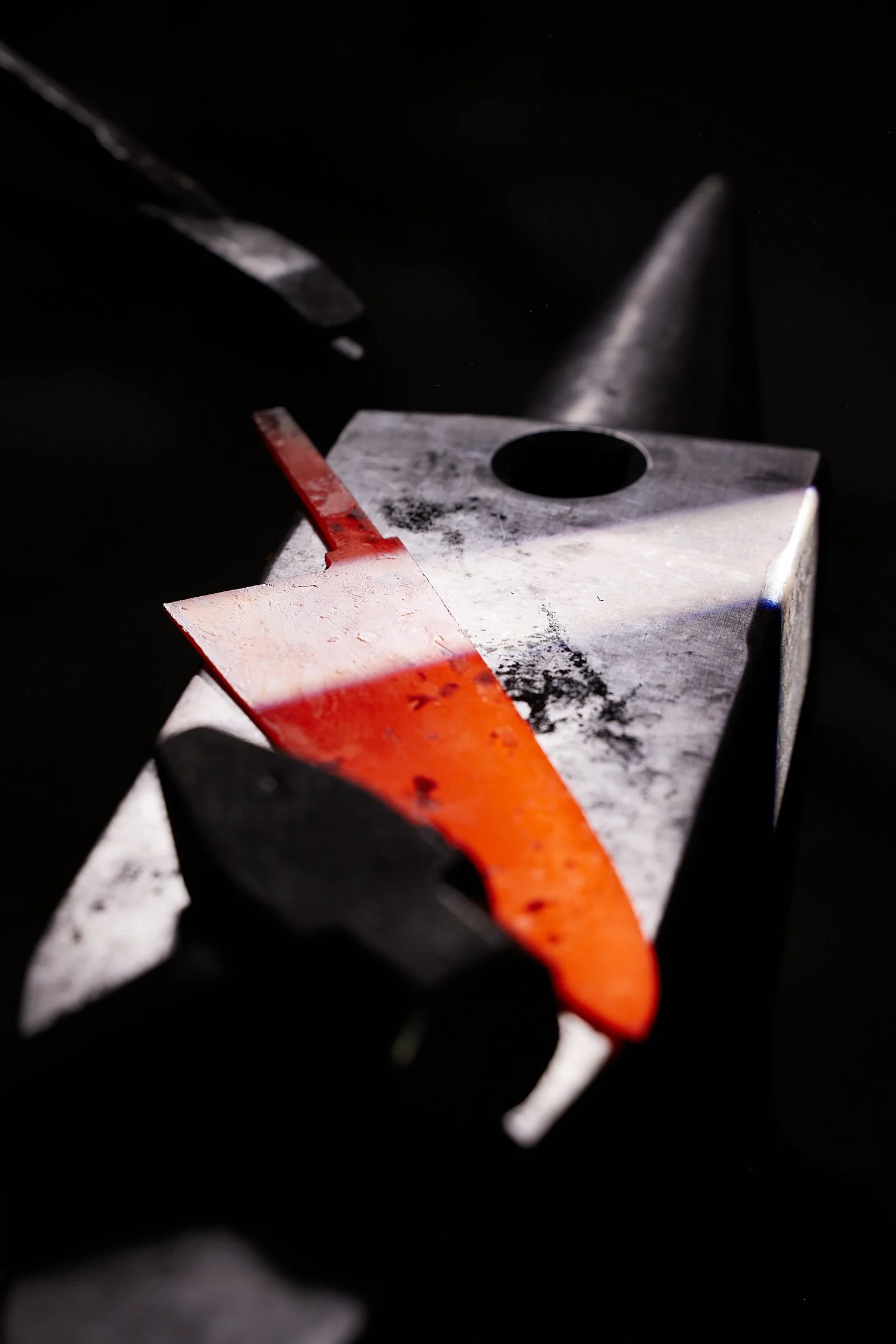 Close-up of a metal tool with a red and orange paint streak on a black background.