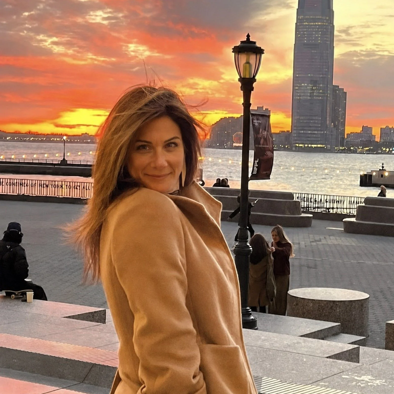 Amy Fisher smiling near the water at sunset with a city skyline in the background.