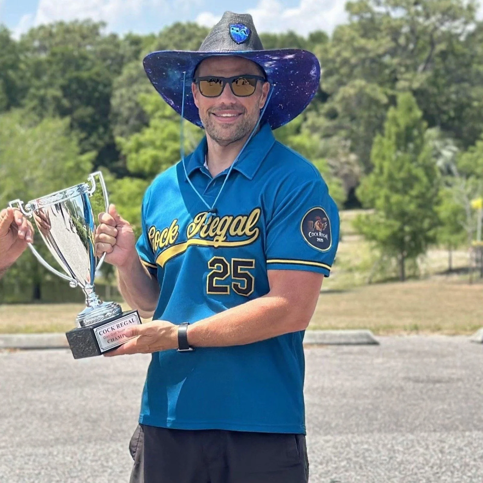 Michael Fisher smiling outdoors while holding a disc golf trophy.