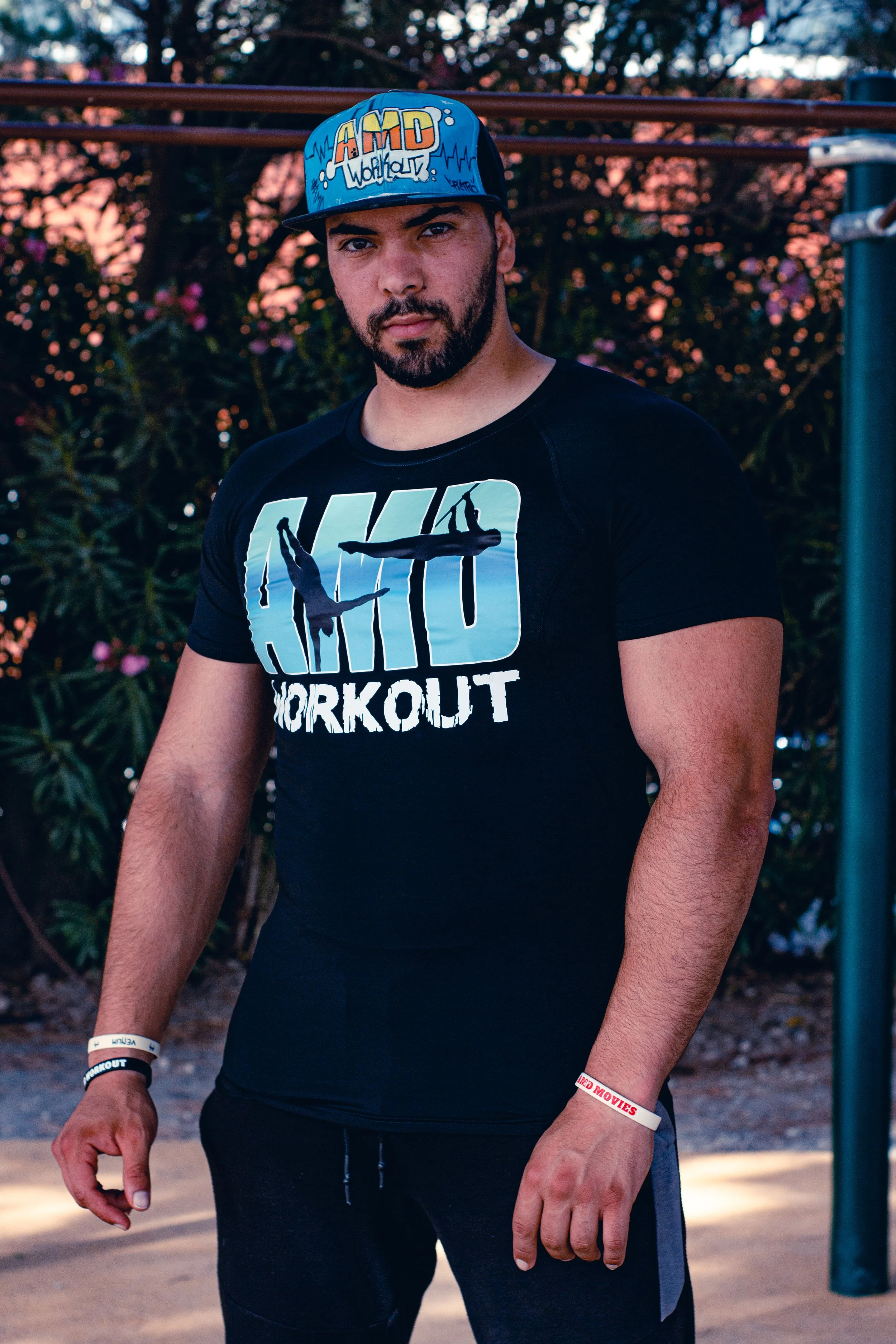 Jeune homme en vêtements de sport avec chapeau à casquette, portant un t-shirt noir avec un logo écrit 'Aero Workout' avec deux danseurs, en extérieur au crépuscule.