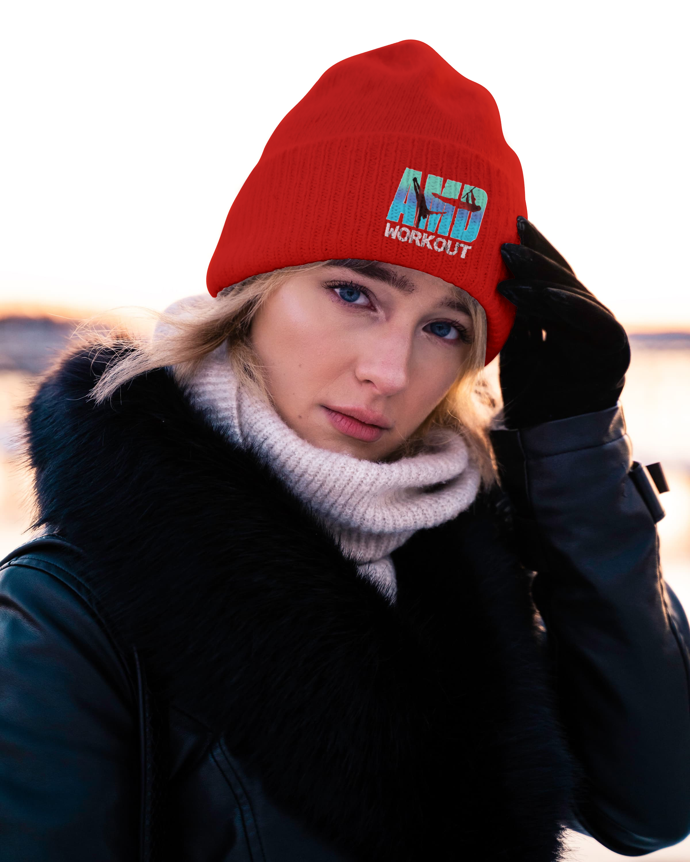 Femme portant un bonnet rouge avec un logo 'AFD Workout', un manteau noir avec un col en fausse fourrure et un cache-col gris, regardant l'objectif lors du lever ou coucher du soleil.